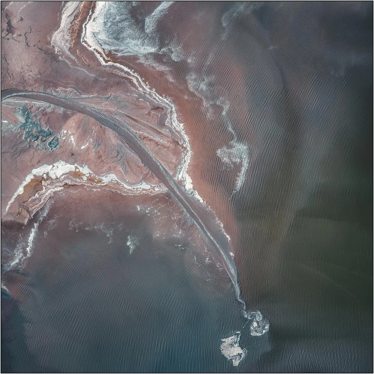 Aerial view of a tailings lake with a curved shoreline and delicate rippled patterns