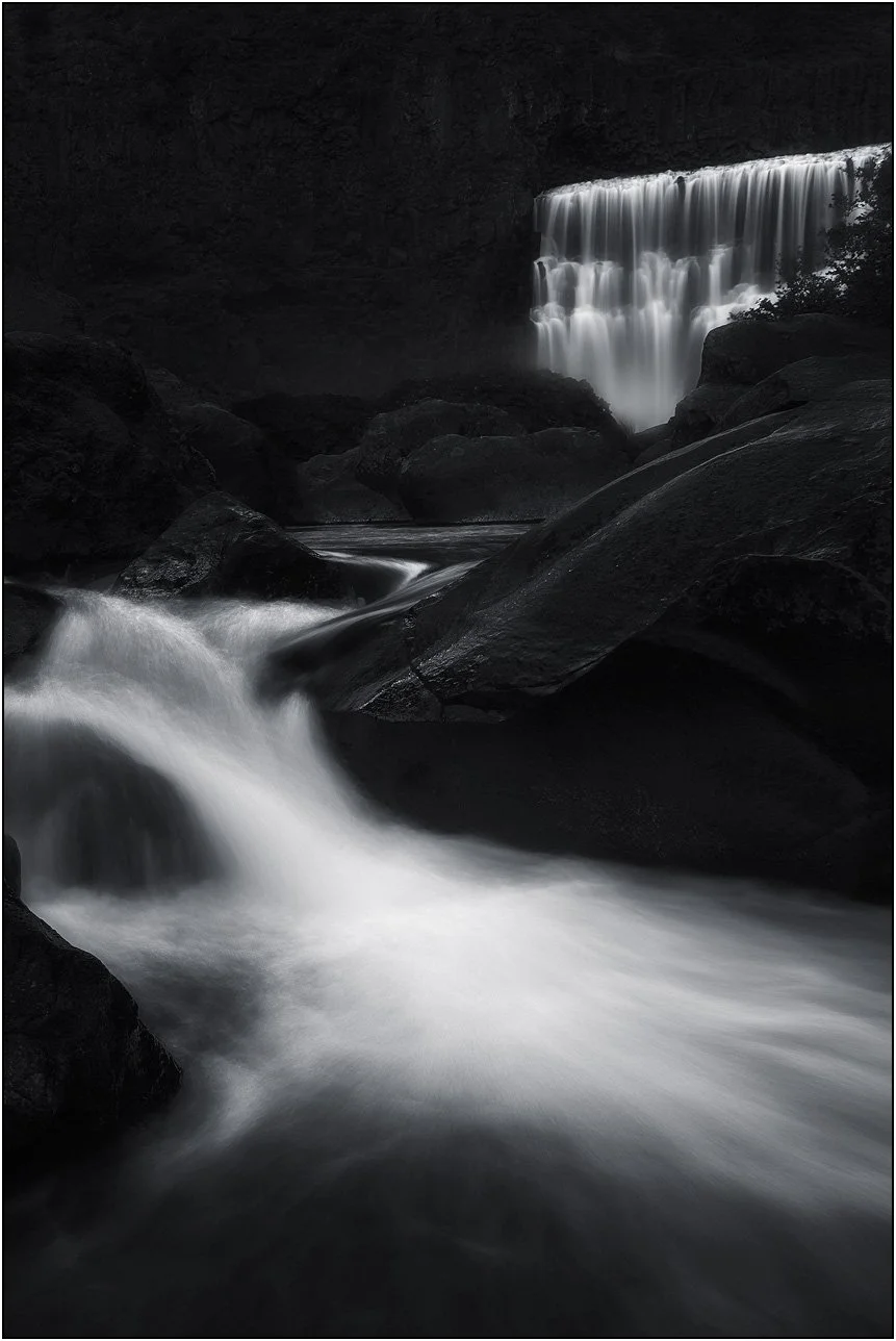 Long exposure waterfall in a dark rocky setting with smooth flowing water in black and white