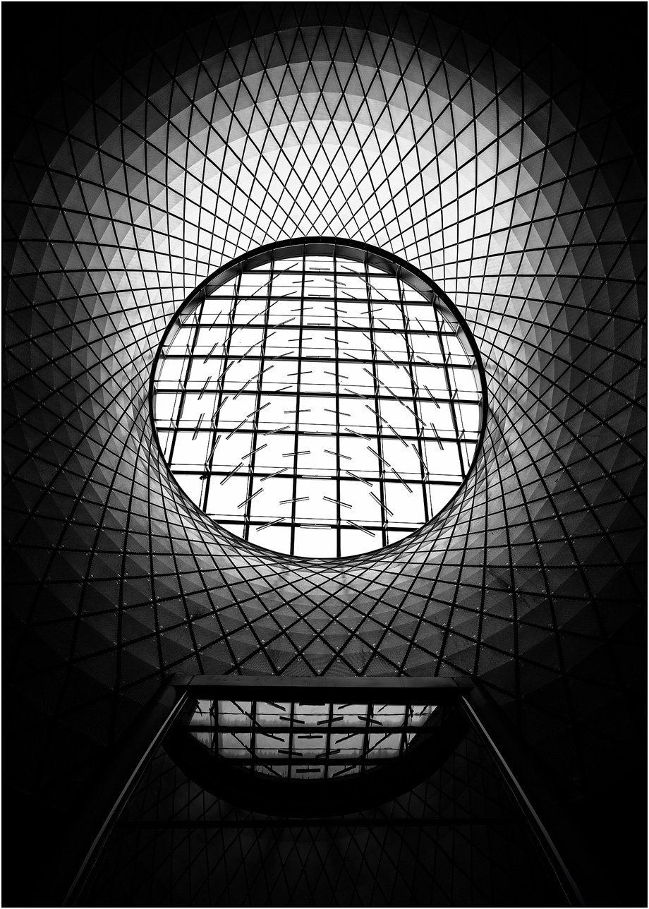 Symmetrical architectural dome with a circular skylight and intricate geometric grid pattern in black and white