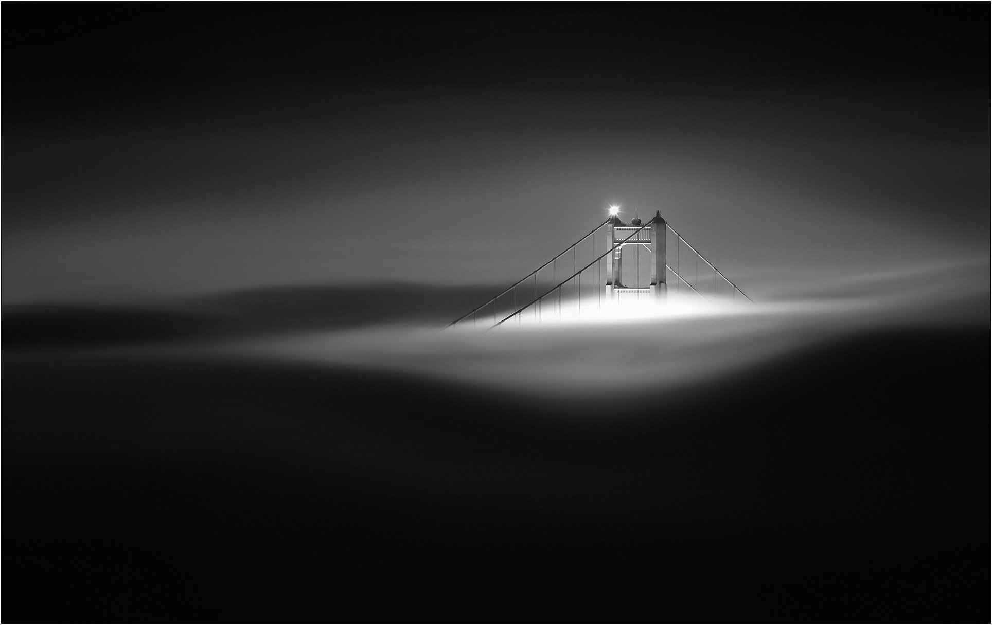 Golden Gate Bridge tower partially hidden in dense fog with minimal light