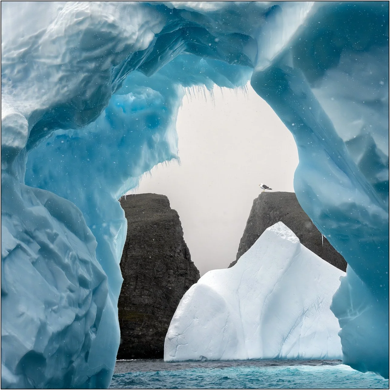 An iceberg arch frames other icebergs rocks in Antarctica peninsula. 