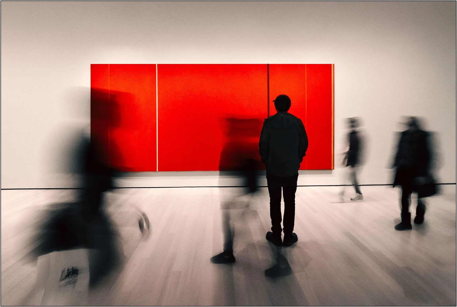 A person standing before a large red abstract painting while blurred figures pass by