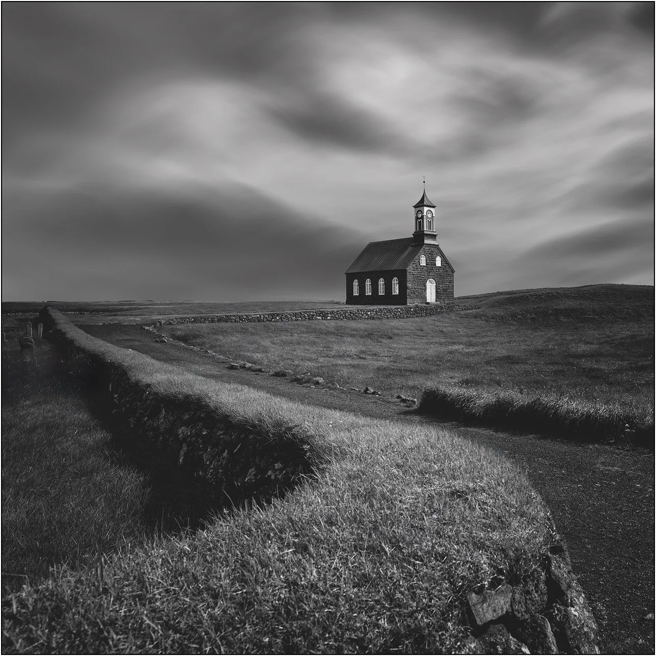Black and white image of Hvalsneskirkja, Iceland, with curve shaped grass walls and smooth soft sky.