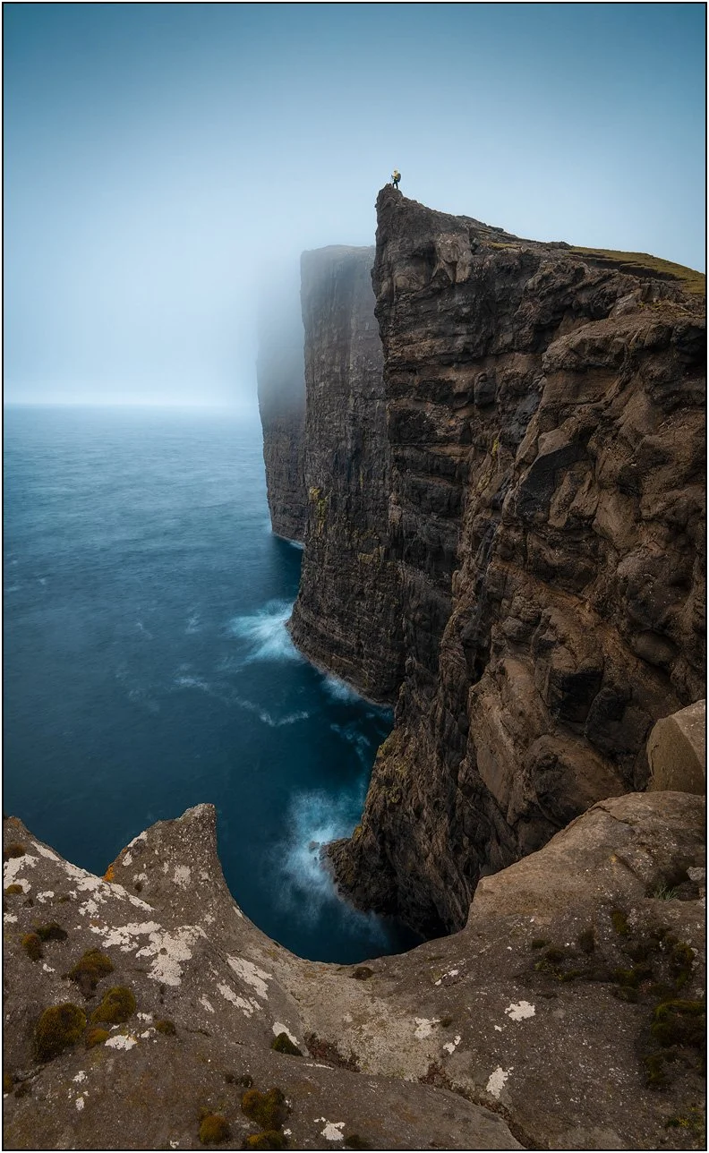 Cliffs near Lake Sorvagsvatn, Vagar, Faroe Islands, with a woman on top of the cliff and ocean water at the bottom of the cliff.