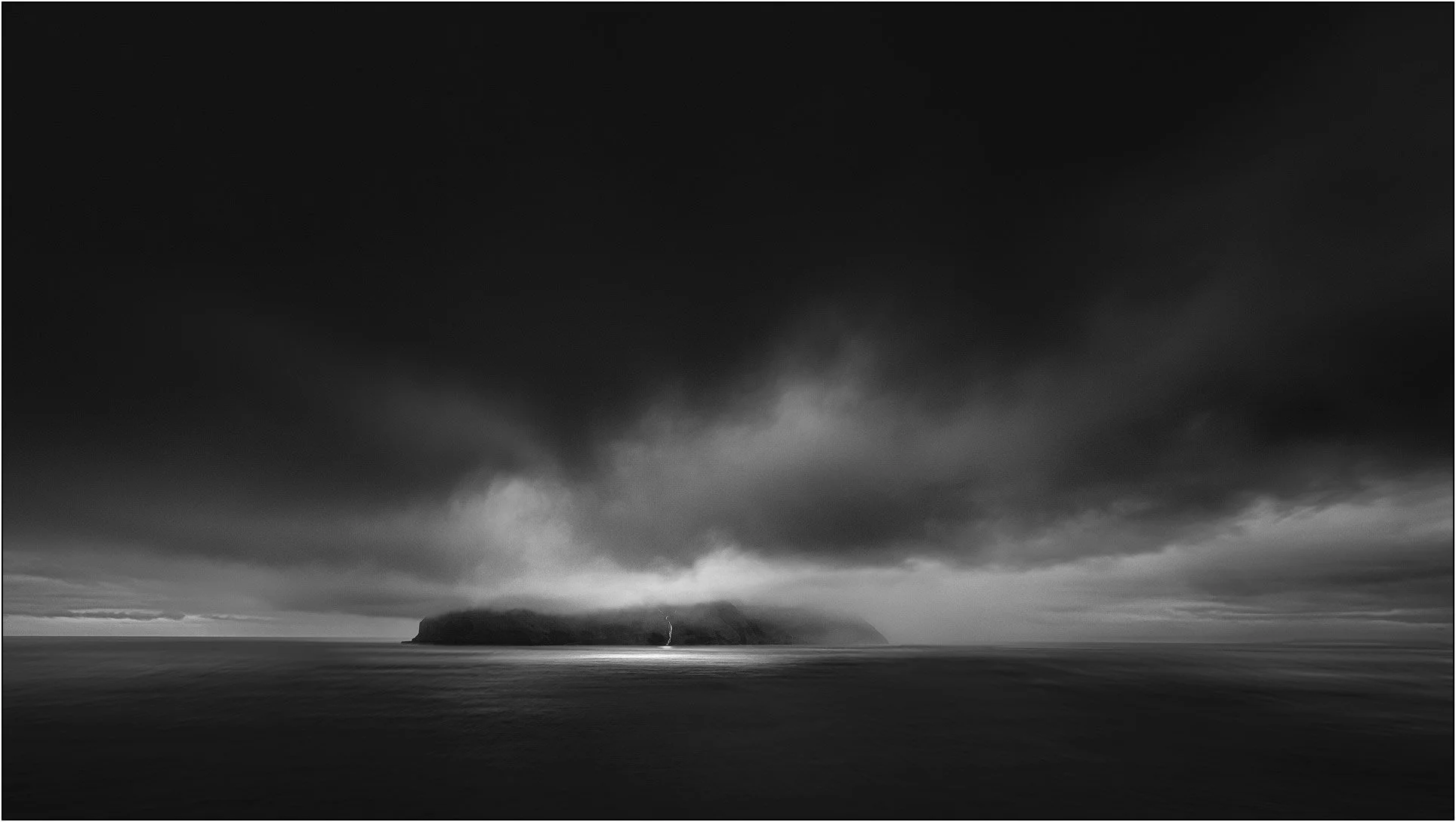 Black and white image of moody clouds over a small island in Faroe Islands.