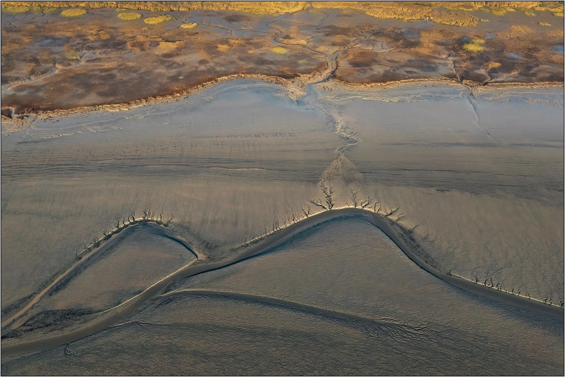 Aerial view of tidal patterns forming gentle curves and layered textures across a tranquil surface