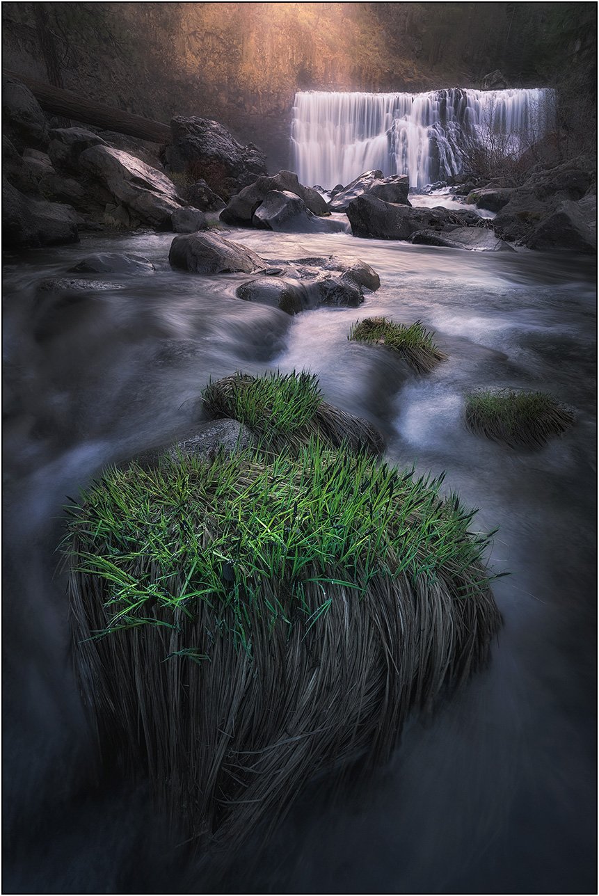 Flowing stream leading to a waterfall surrounded by rocks and soft light