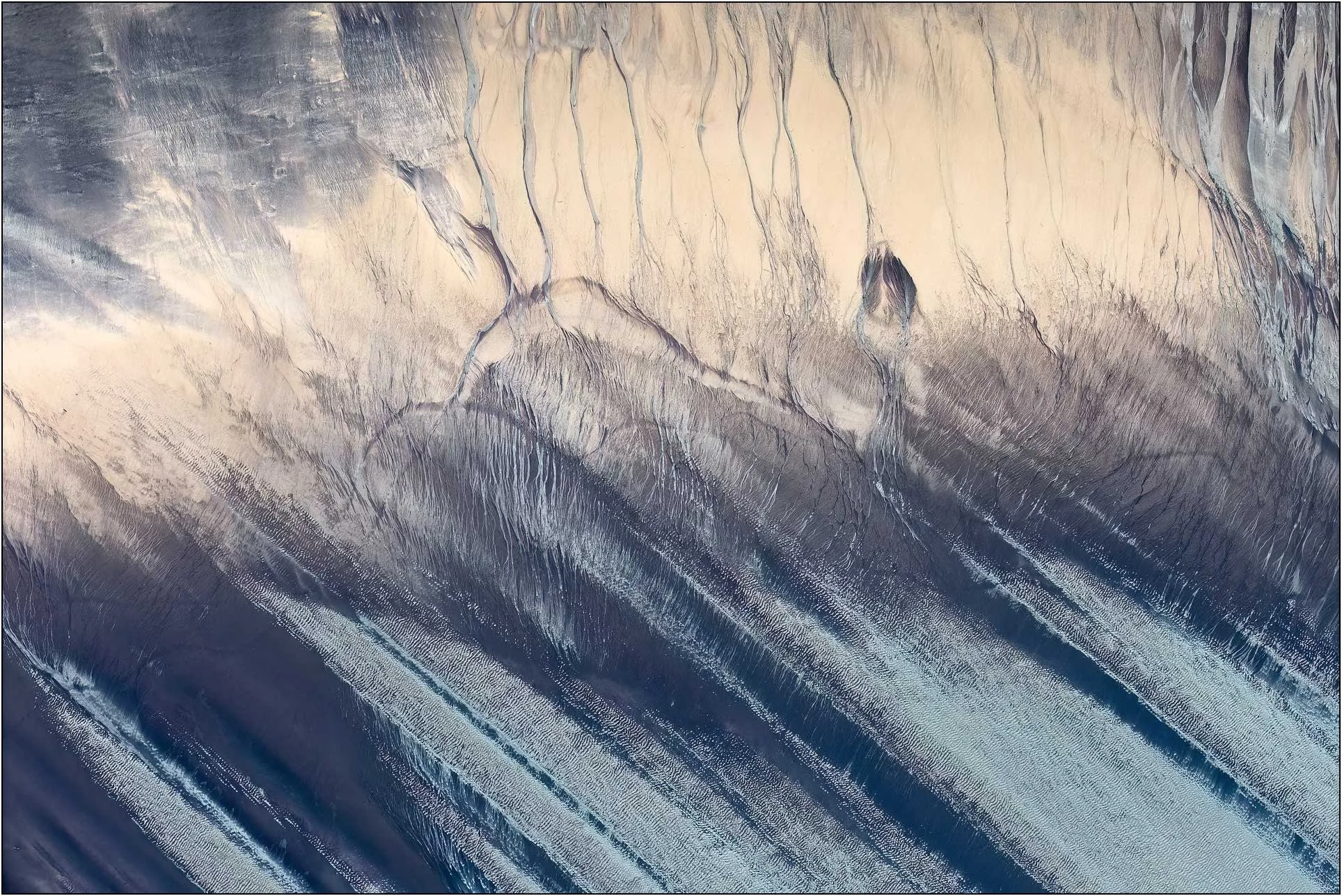 An aerial view of the Qiantang River tidal flats in China, where tidal currents sculpt layers of sand and sediment into sweeping lines and delicate branching patterns. The flowing textures evoke mountains, rivers, and an imagined landscape, turning t