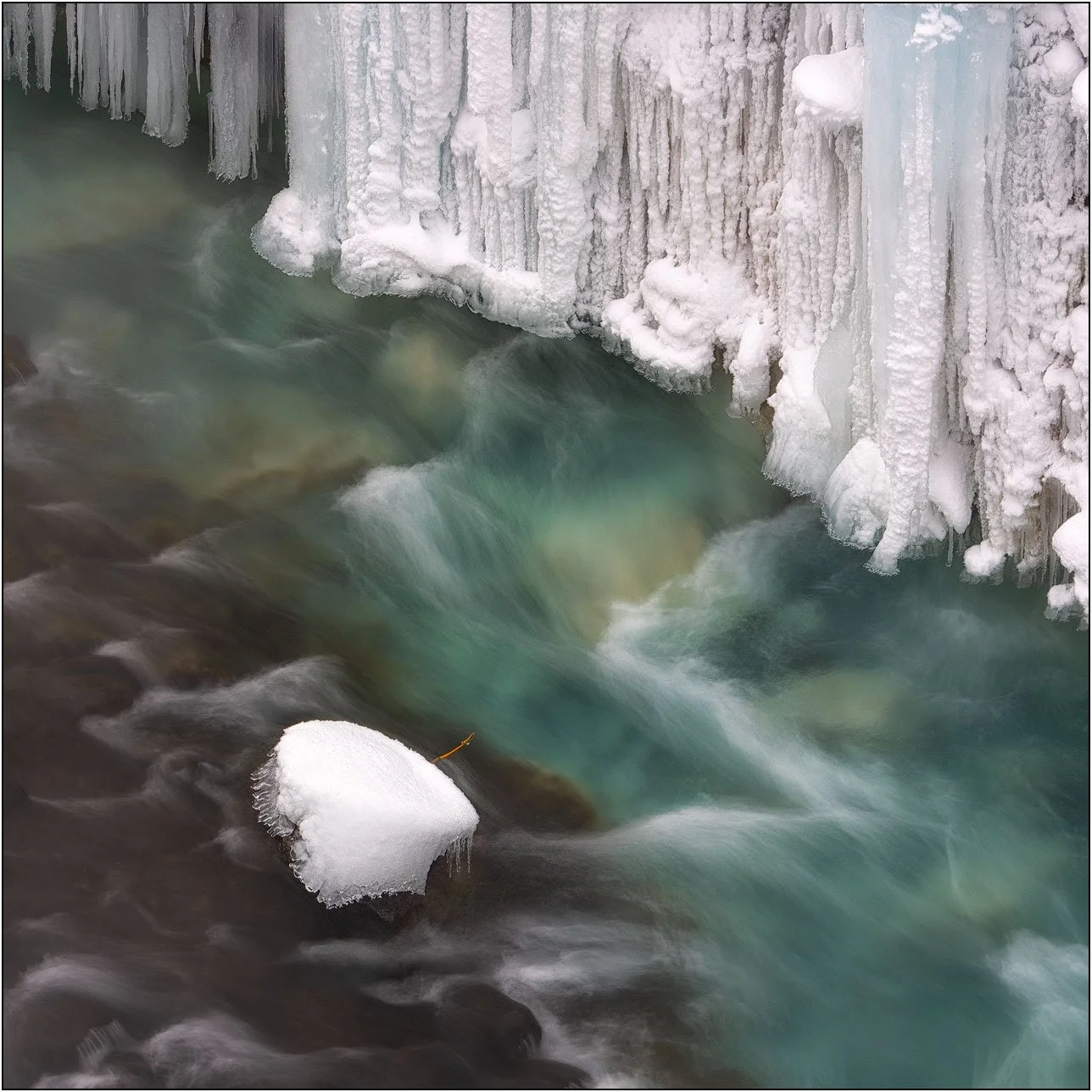 Frozen icicles forming along Shirahige Waterfall with flowing water beneath in winter, Hokkaido, Japan.