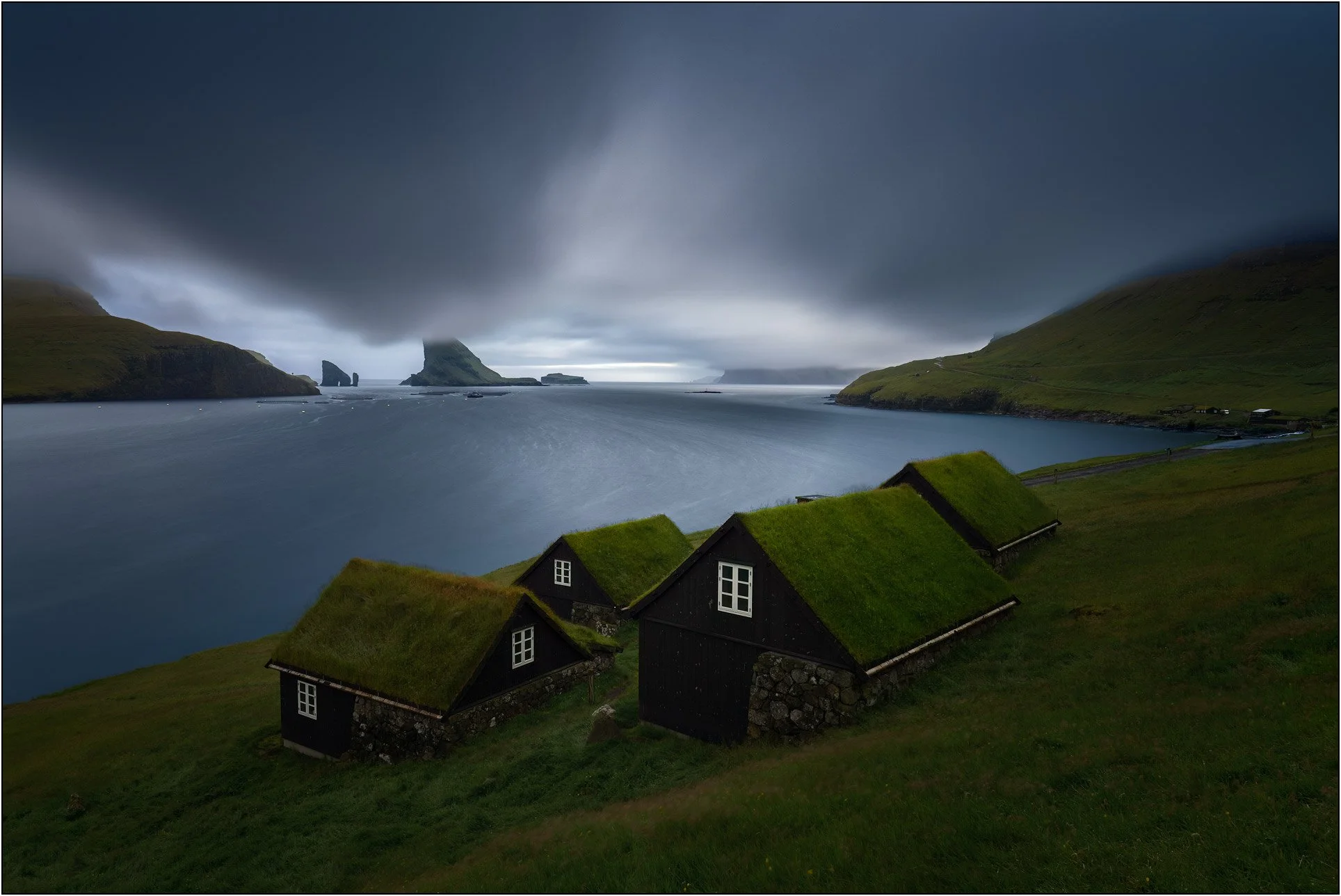 Long exposure landscape of Bøur View, Faroe Islands, with grass covered houses, fjords, islands, and long exposure water and clouds.