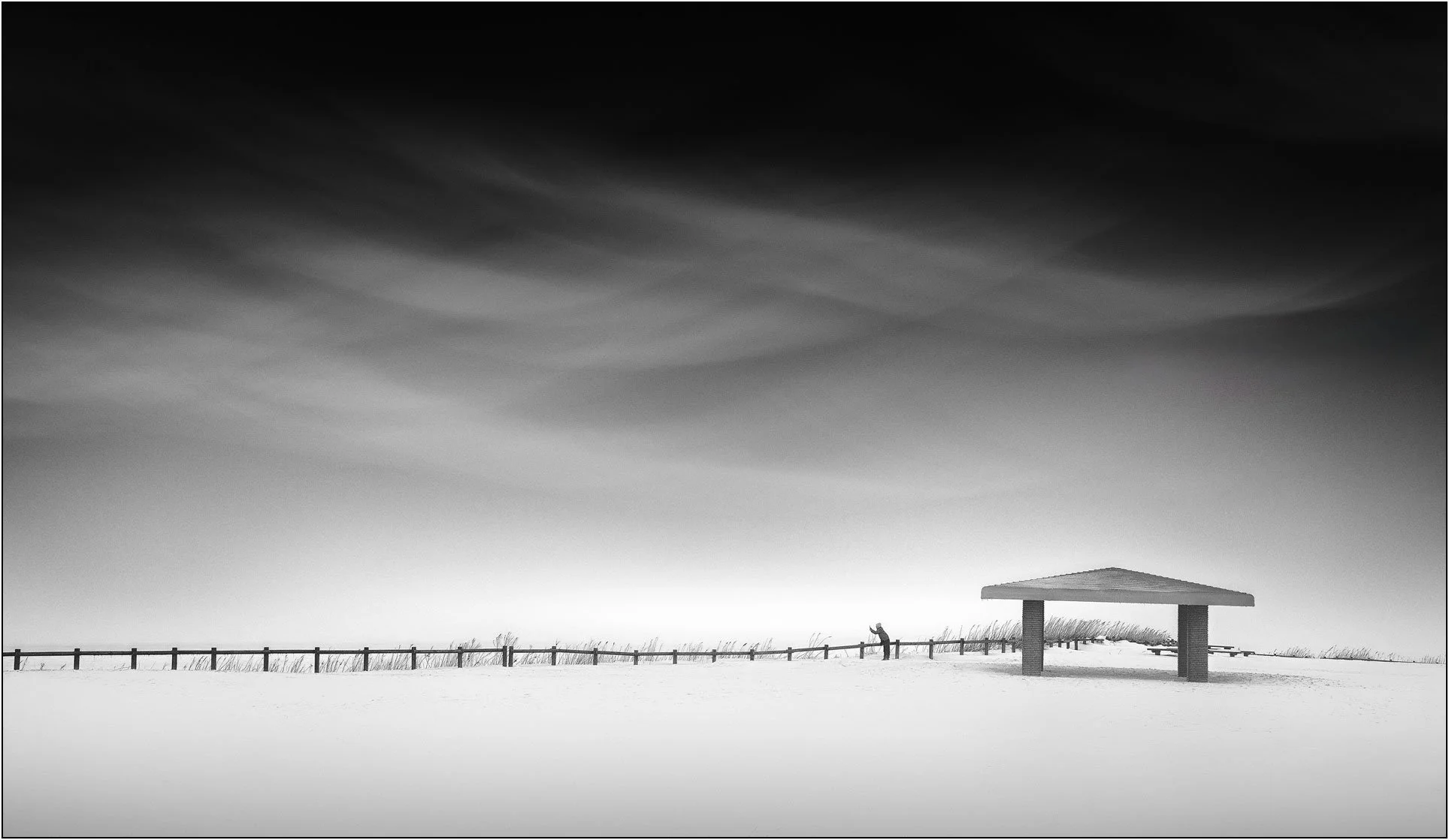 A minimal winter landscape with a small shelter and a lone person in a vast snowy field in Hokkaido, Japan.
