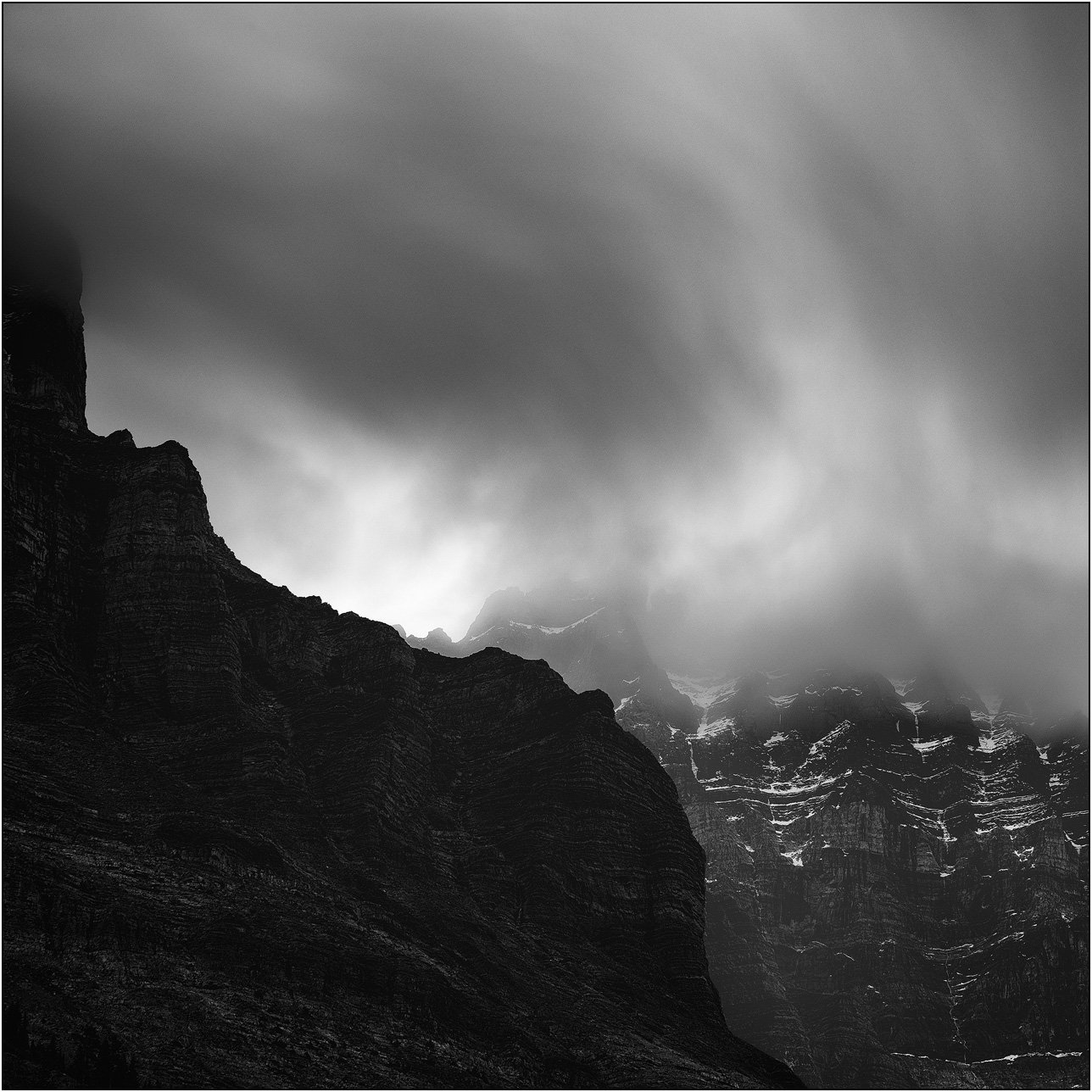 Black and white long exposure photograph of cloud and peaks of the Canadian Rockies.