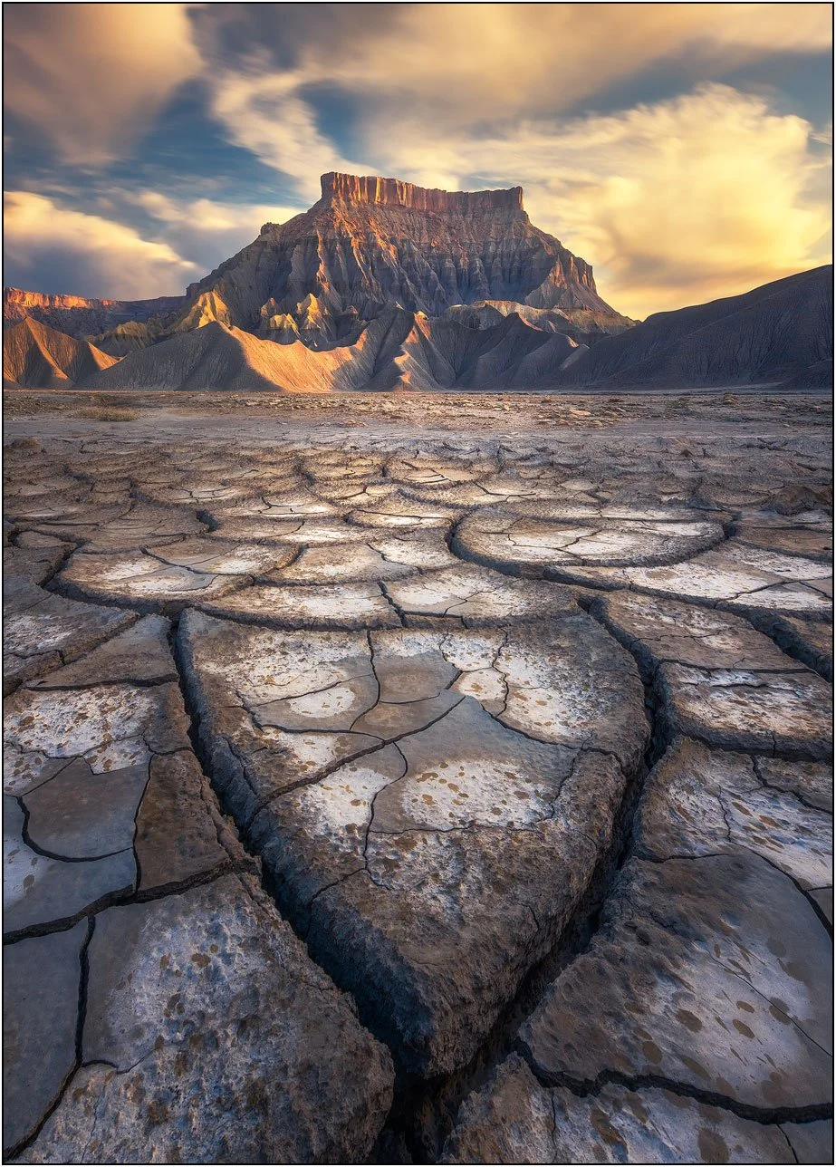 Cracked mud foreground leading to dramatic desert butte under cloudy sky in Utah badlands