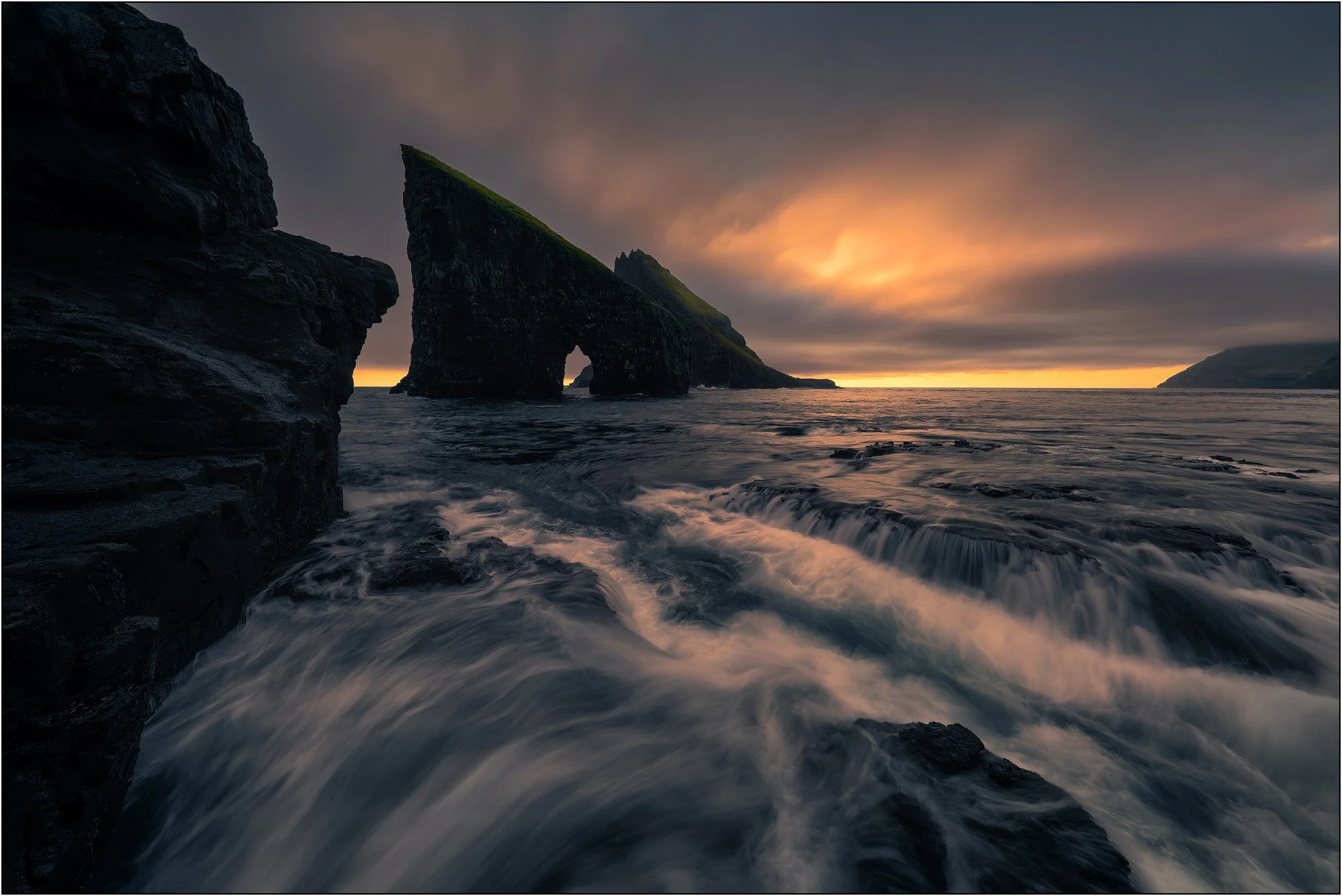 Waves crushing on island of Drangarnir, Faroe Islands, with sunset clouds, golden light and sea stacks.