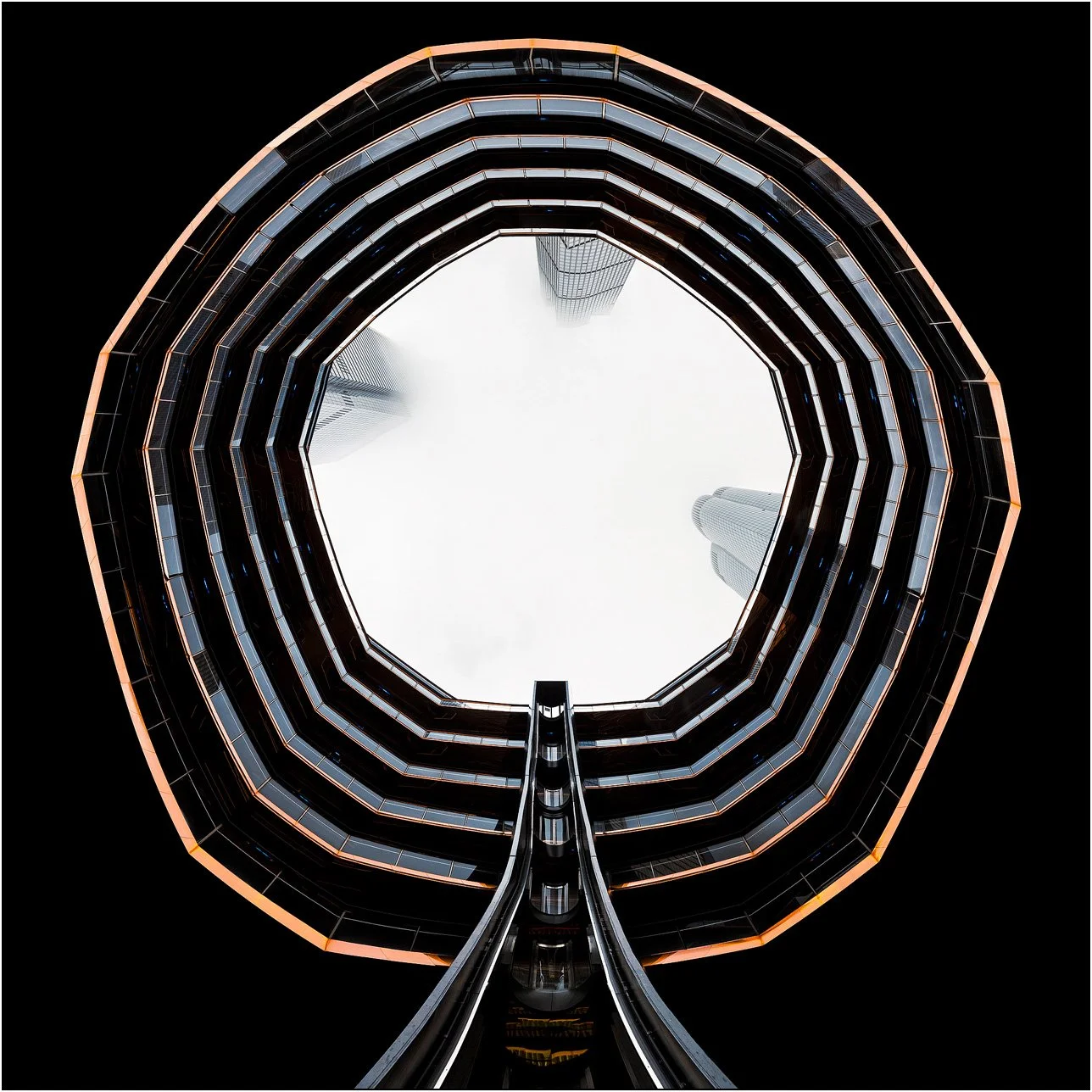 Upward view of the Vessel structure in New York forming a circular architectural frame against the sky, viewing buildings in fog.