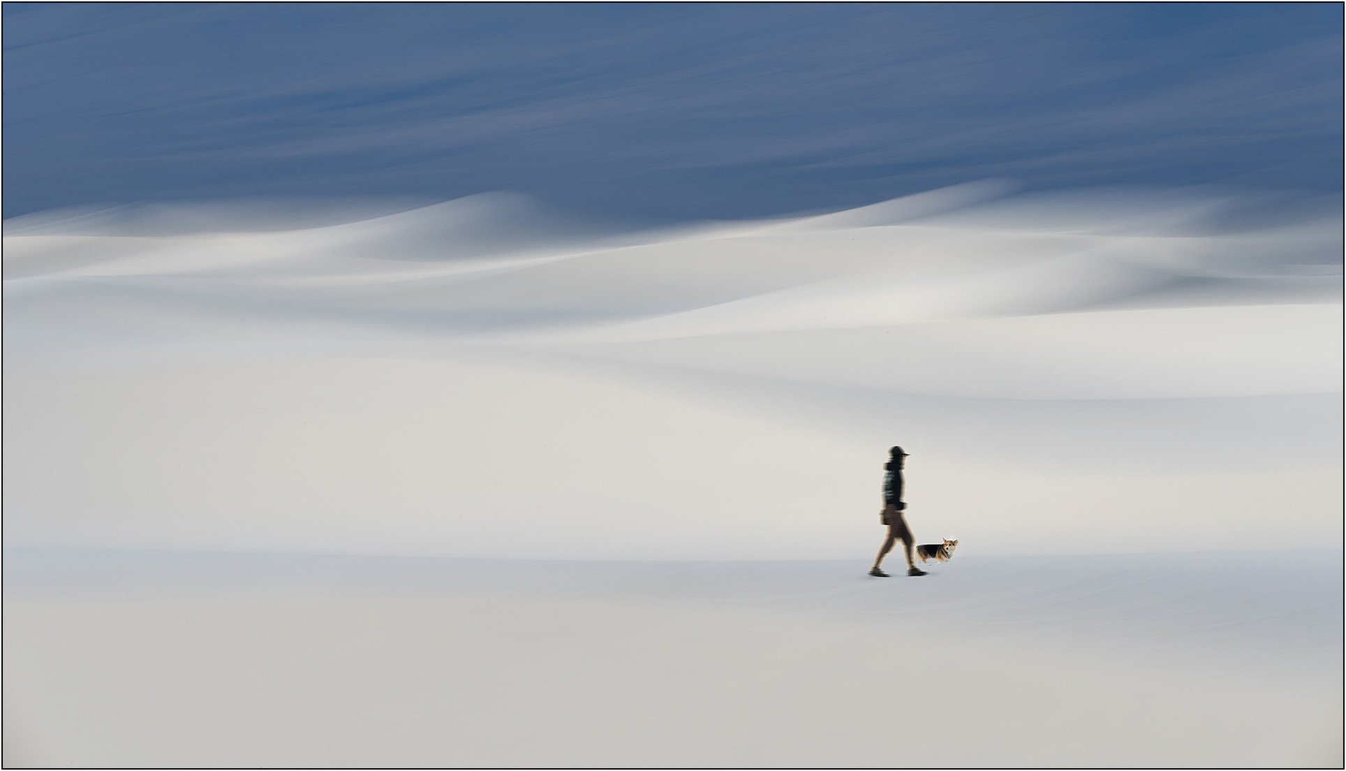 Slightly blurred woman and dog walking on white sands with a soft blurry background.