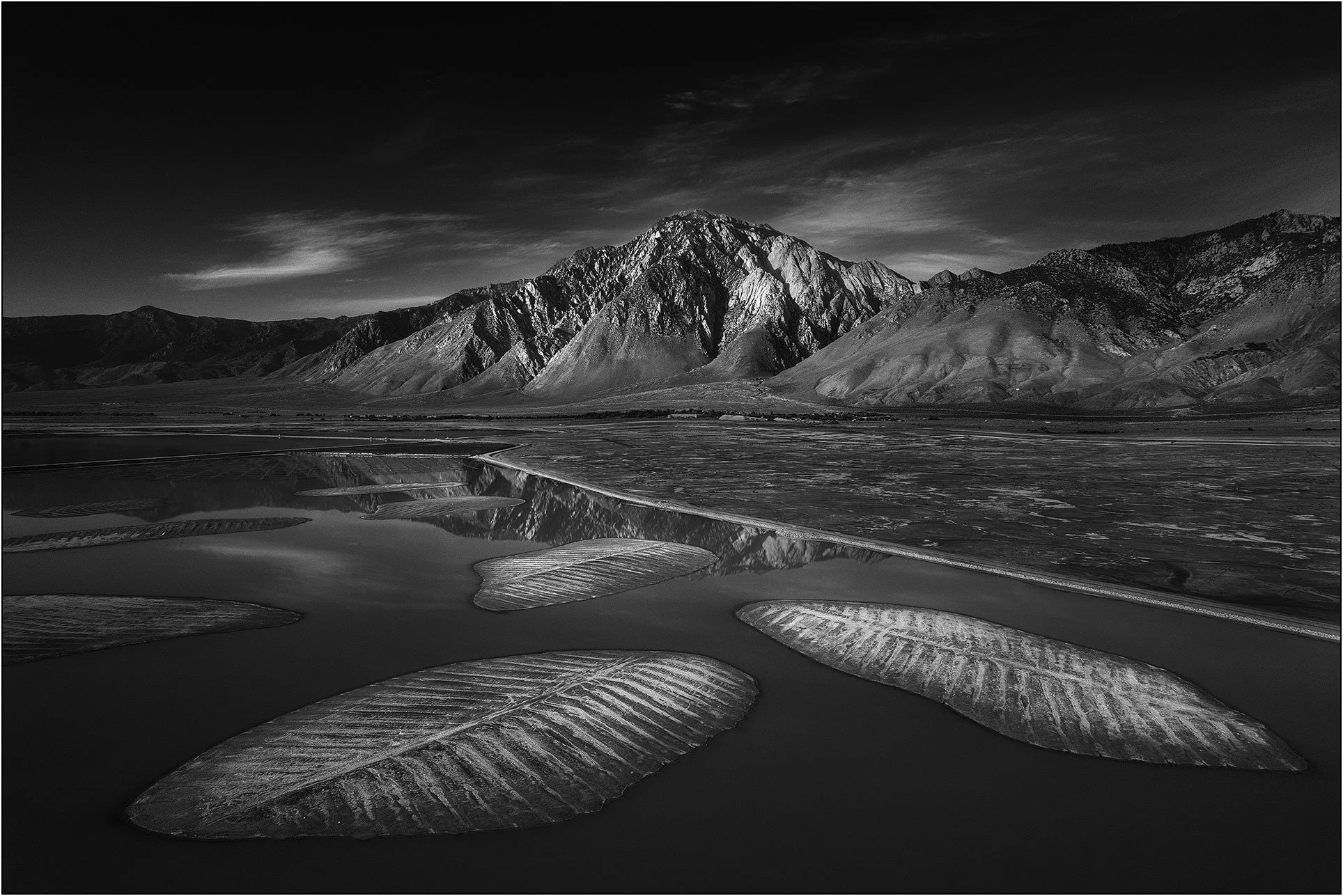 Black and white mountain landscape with reflective water and textured foreground