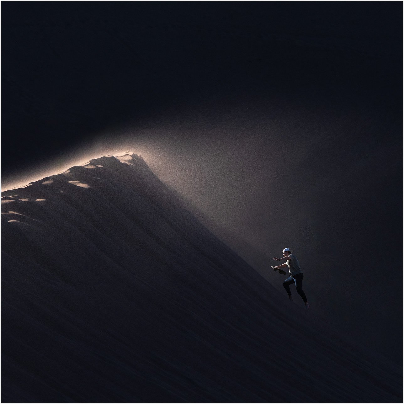 A person climbing a sand dune ridge with wind and light illuminating the crest