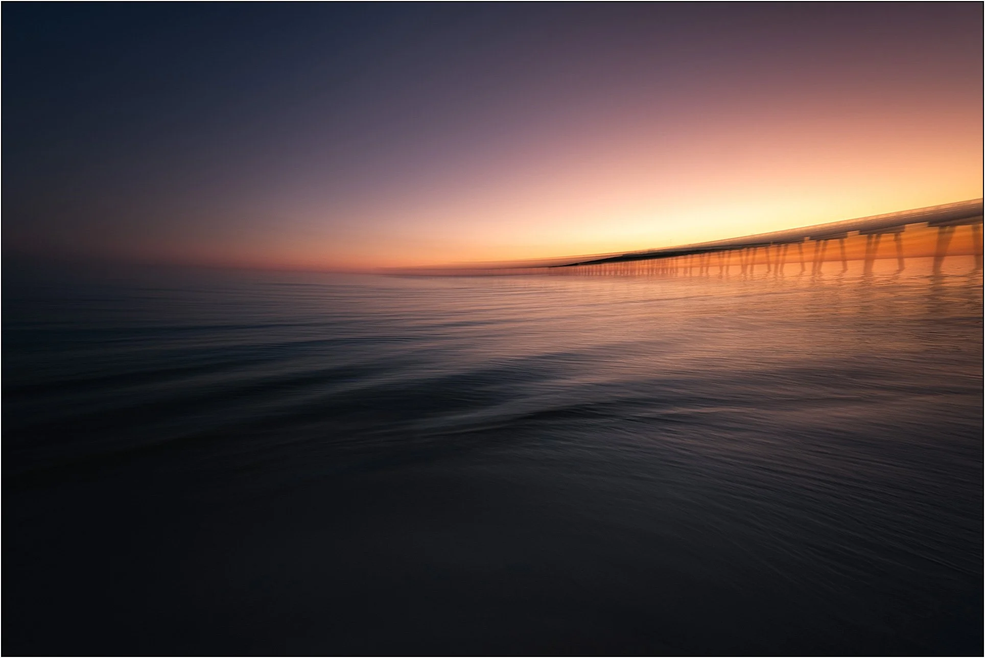 Long exposure seascape with blurred water and a pier extending into a soft glowing horizon at sunset, Florida.