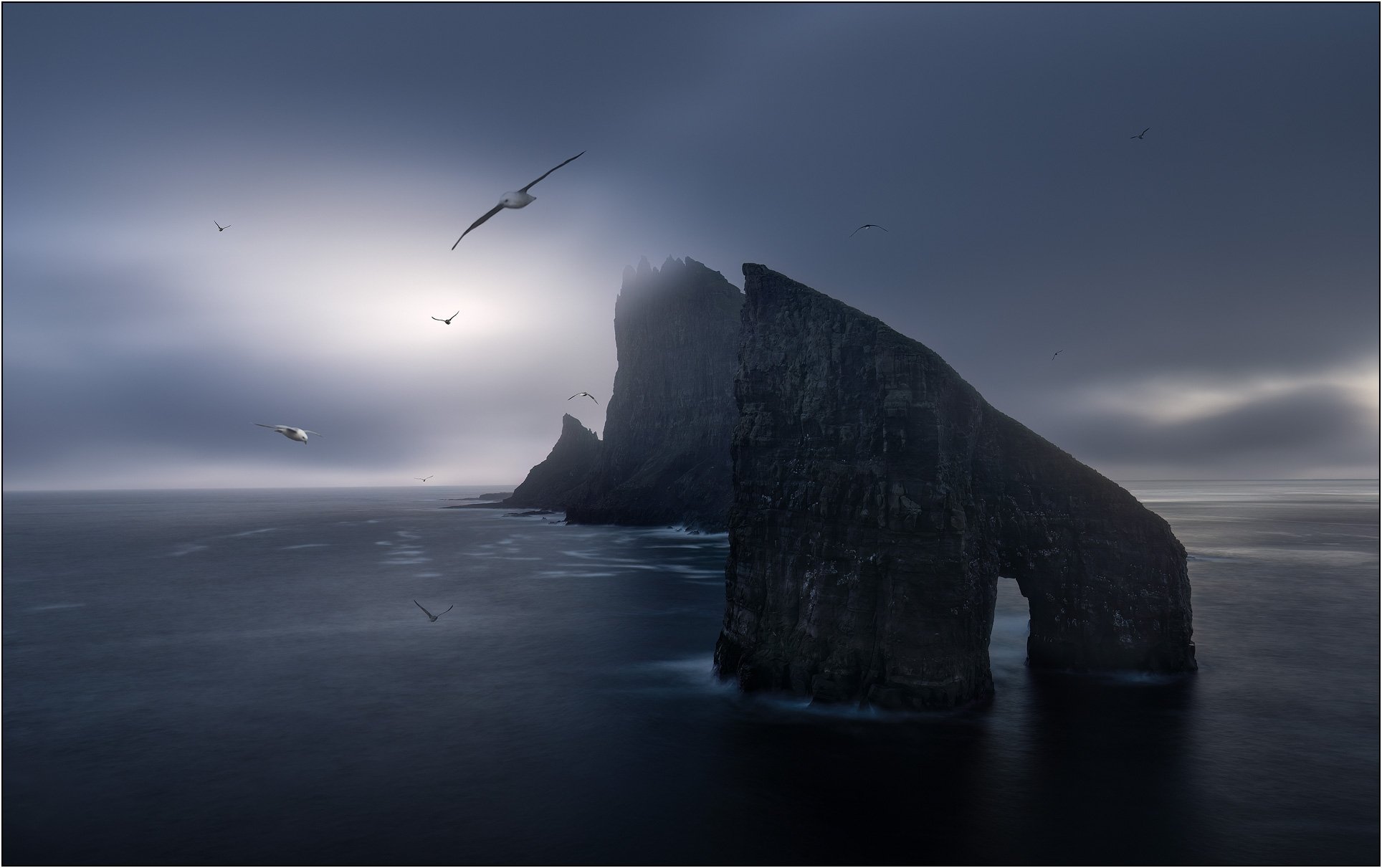 Moody image of sea birds flying over sea stacks of Drangarnir, Faroe Islands.