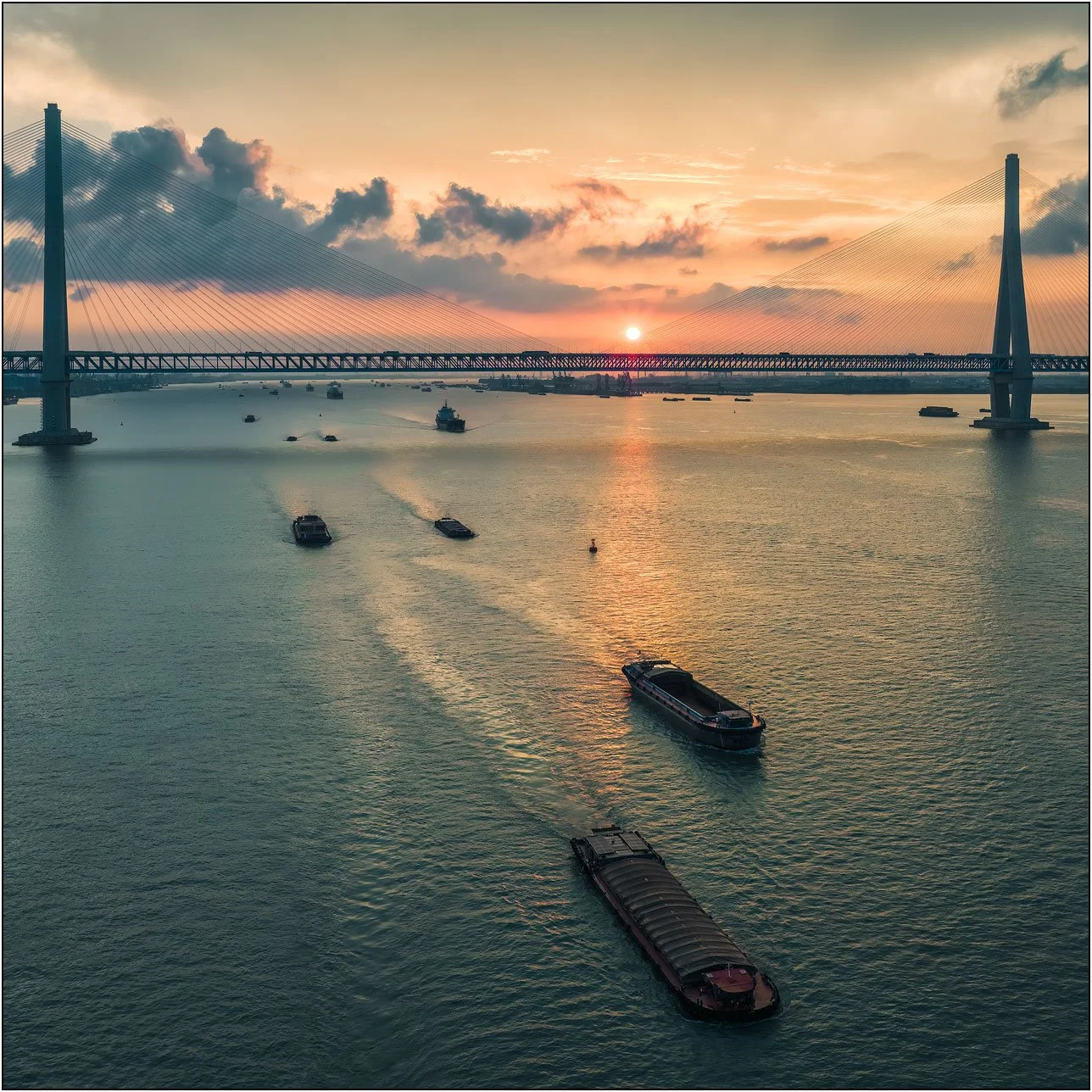 Boats pass under bridge of Yangtze river at sunset in Zhangjiagang, China.