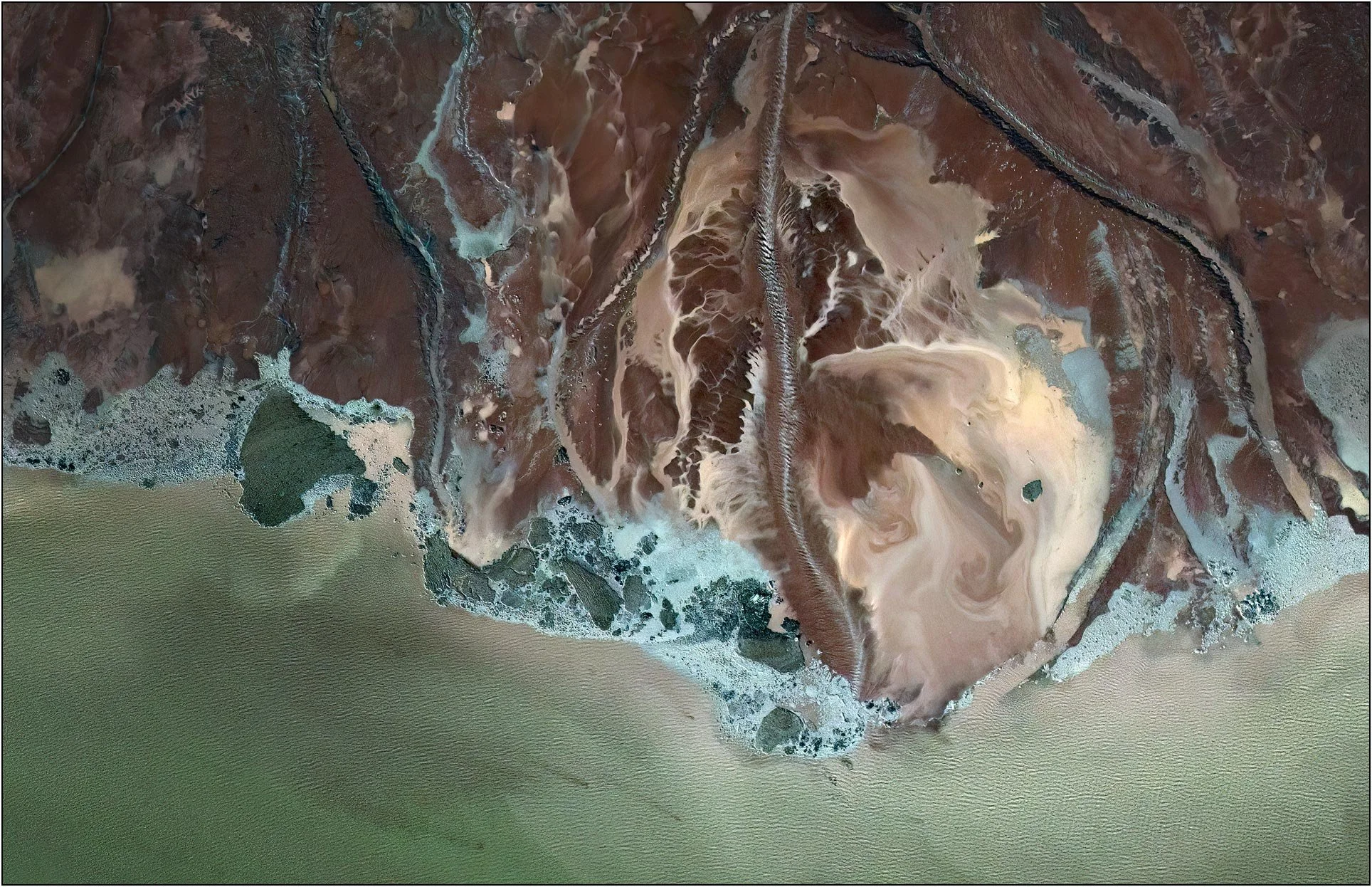 Aerial view of a tailings lake with a horizontal band of turquoise contrasting earthy textures