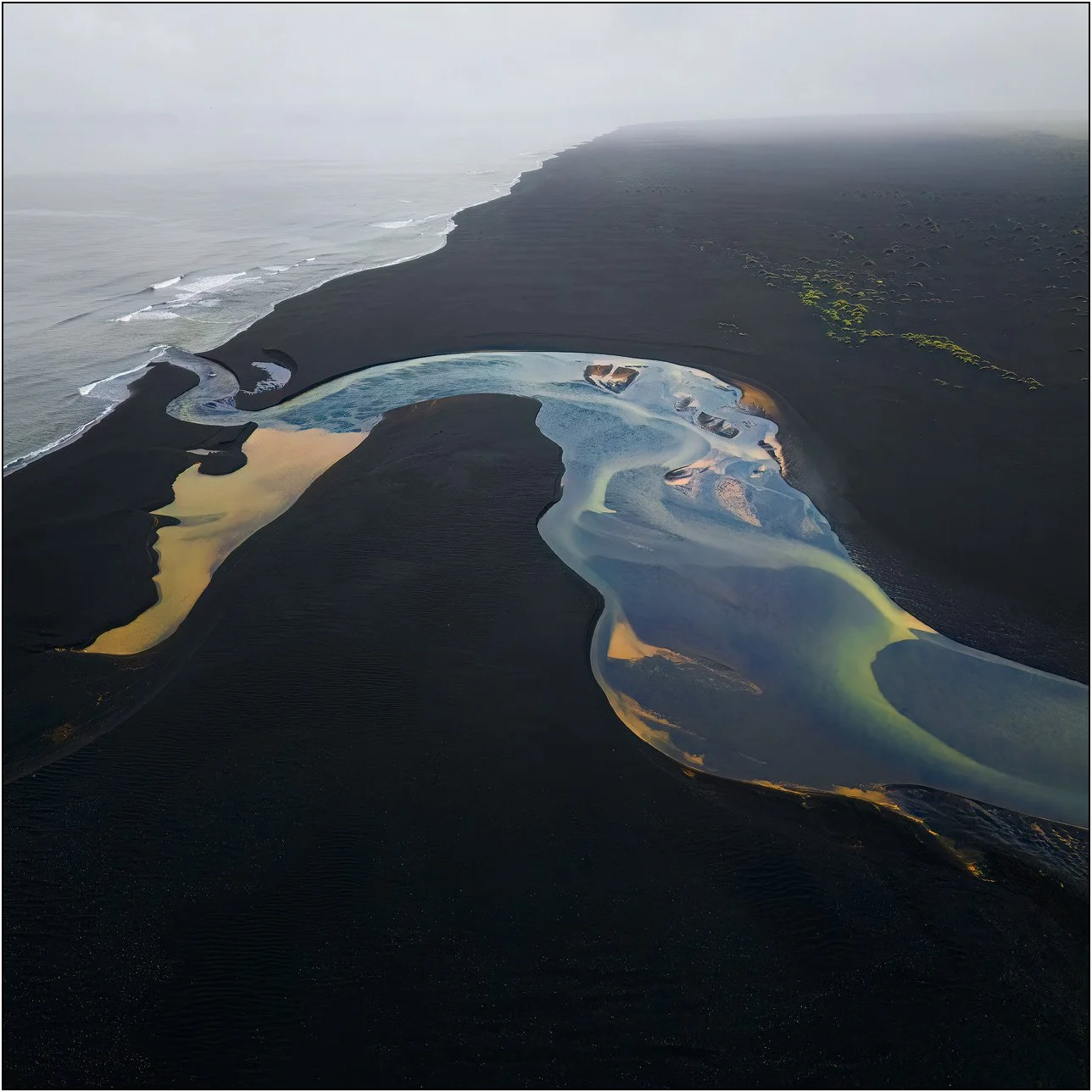 Aerial view of glacial river flowing into the ocean in Iceland, forming colorful abstract patterns.