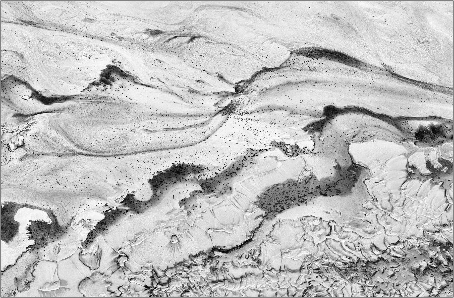 Aerial abstraction of a tailings lake with bold dark textures contrasting against a luminous white ground