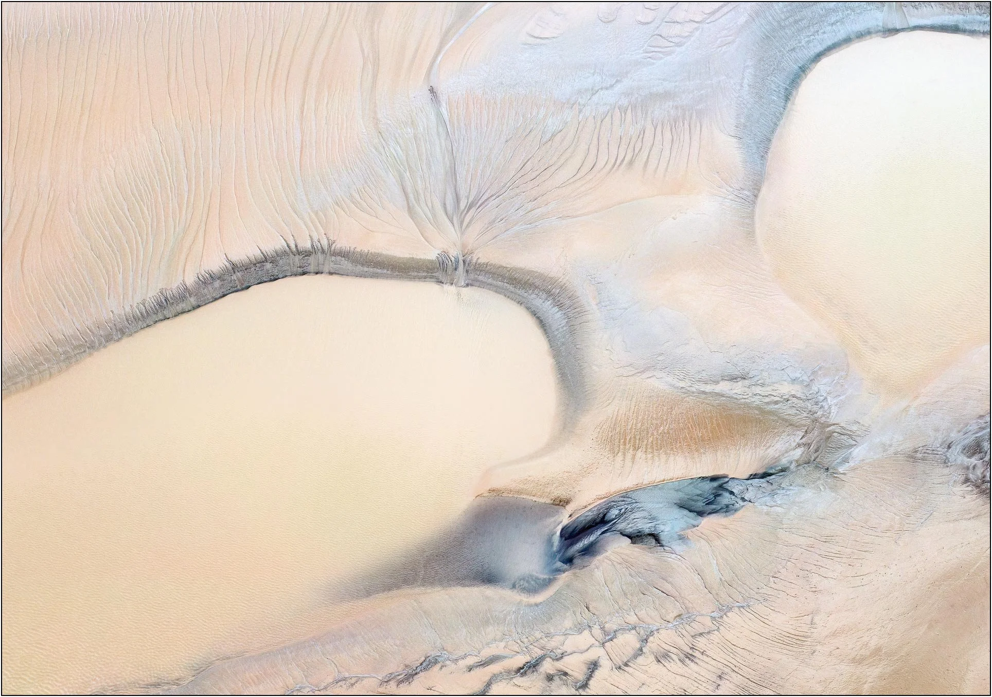Minimalist aerial photography of the Qiantang River tidal flats in China, where receding tides draw graceful curves and delicate branching lines across pale sand. Subtle blue-gray sediment and expansive negative space create an abstract composition w