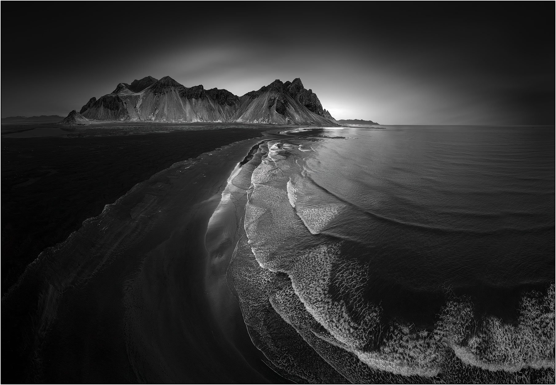 Black and white aerial view of Vestrahorn, Iceland, with curving waves leading to the mountain.