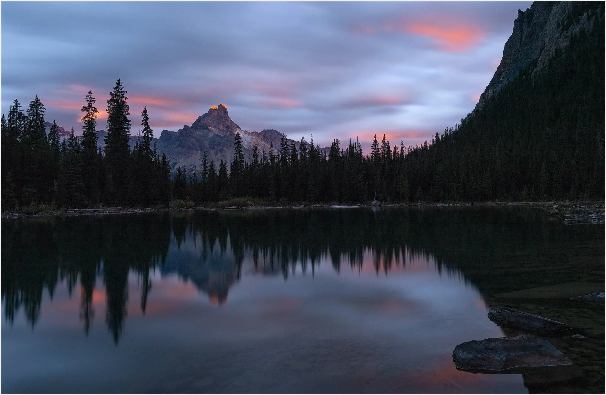 Mountain and forest reflections on calm water at dawn in Lake O'Hara, Canada.