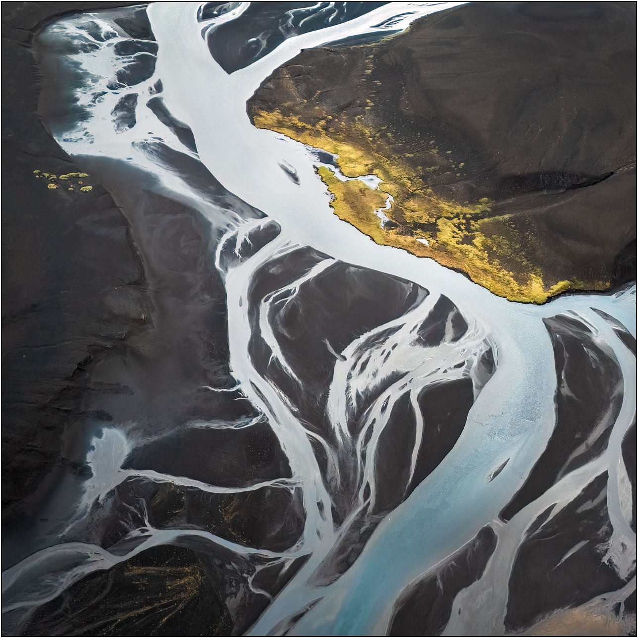 Aerial view of braided glacial rivers flowing through dark volcanic sand, forming abstract patterns with luminous white channels.