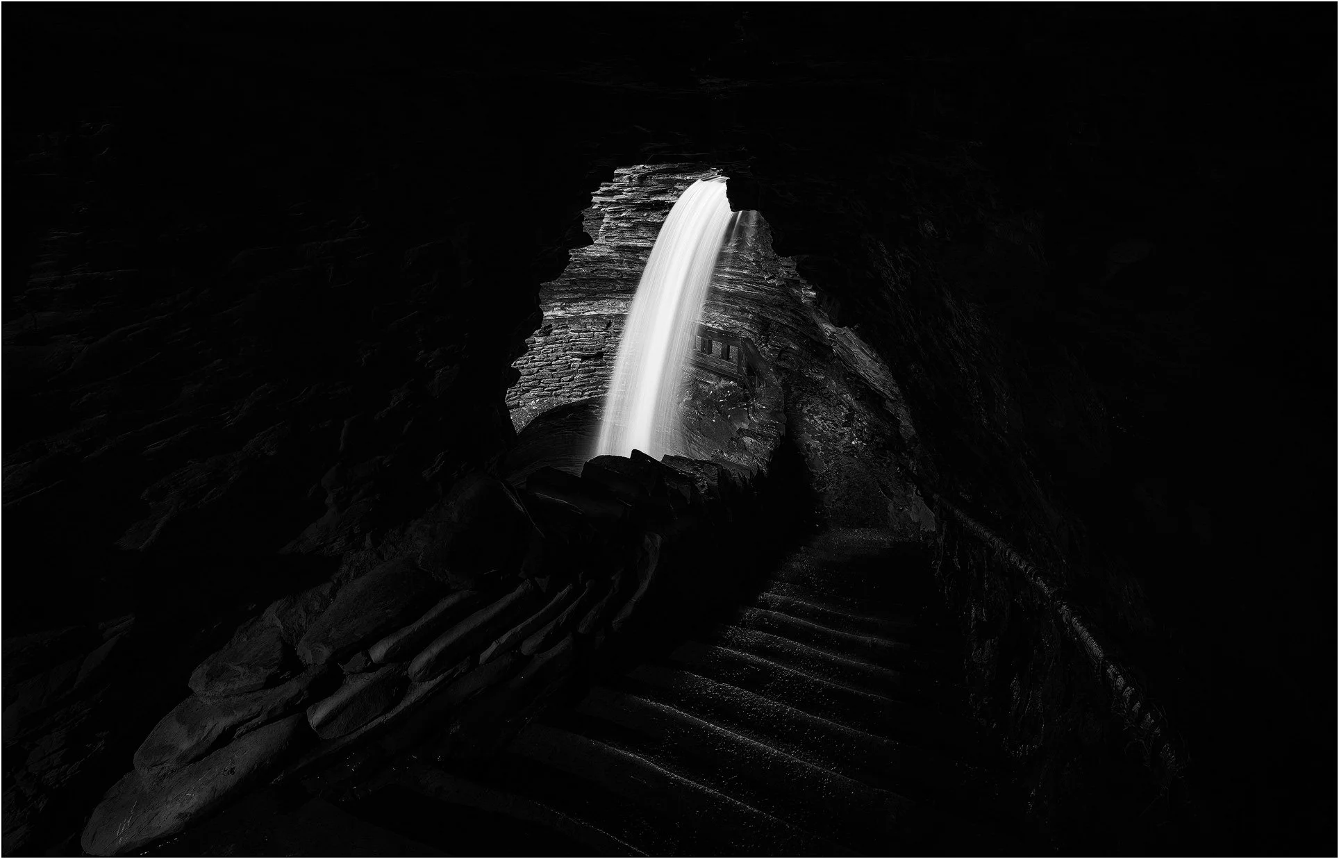 A waterfall illuminated through a dark rock cavern creating a dramatic contrast of light and shadow in Watkins Glen state park