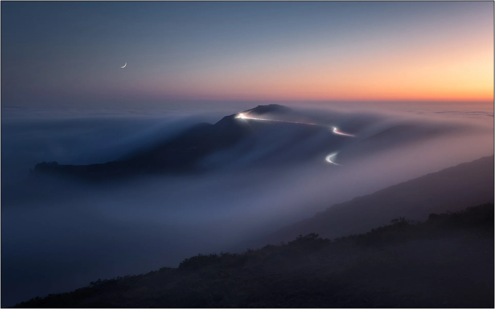 Winding road lights cutting through rolling fog at twilight