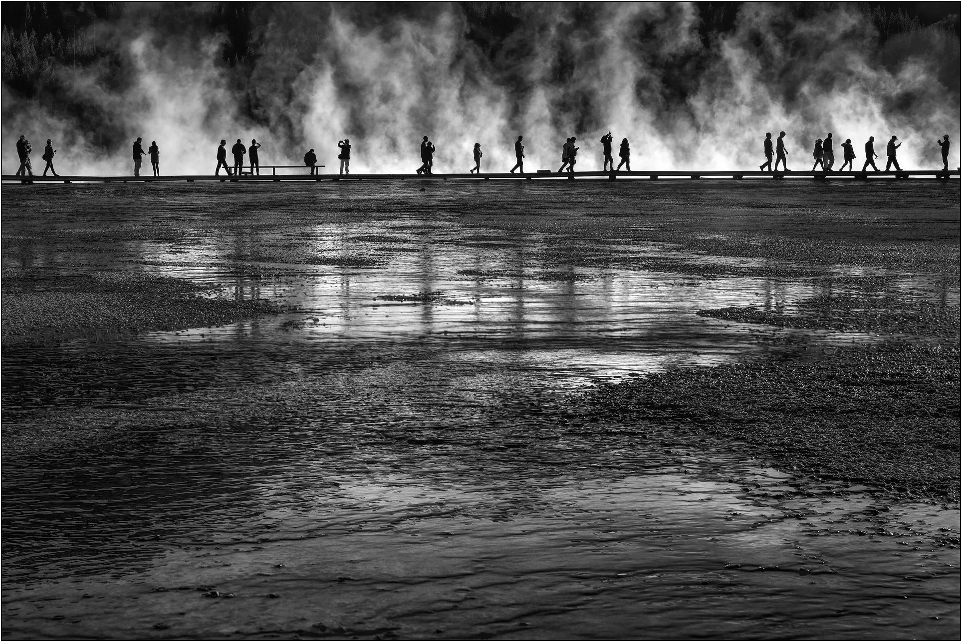 Silhouetted visitors walking along boardwalk through steaming geothermal area in Yellowstone National Park