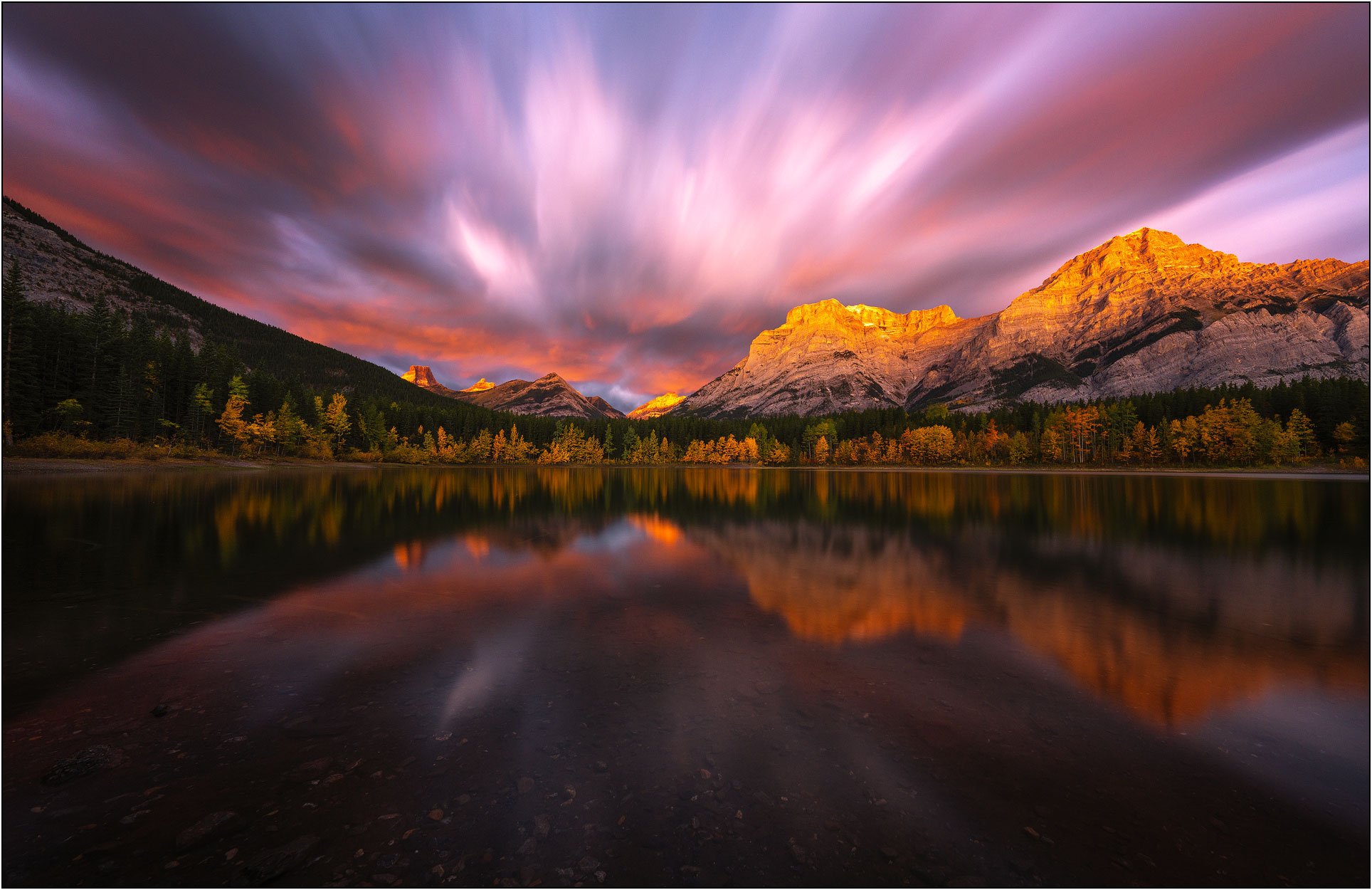 A burning sunrise with golden light at Wedge Pond, the Canadian Rockies. Mountain and fall forest reflections.