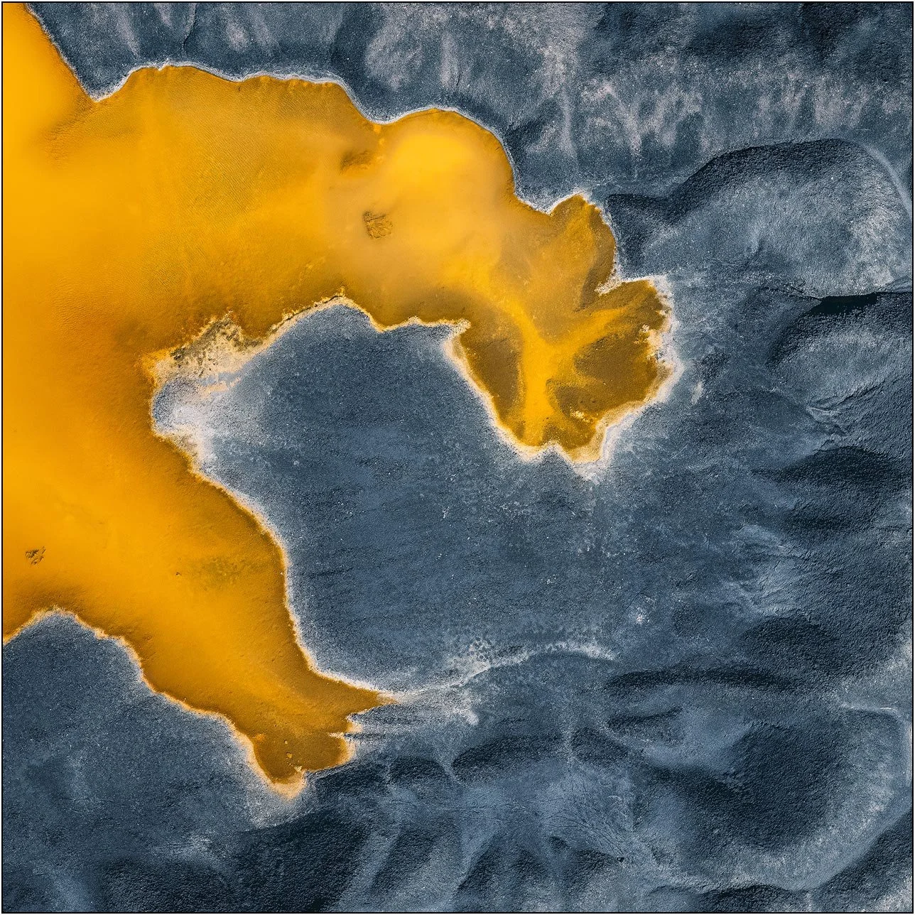 Aerial view of a tailings lake with a bold yellow mineral patch against dark textured ground