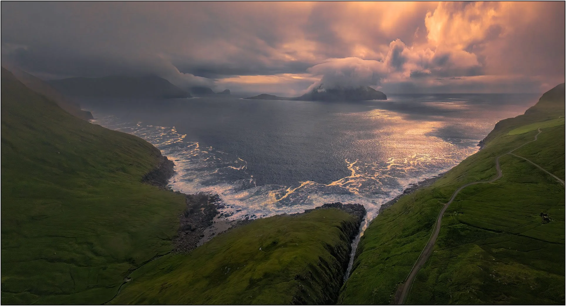 Panoramic aerial view at sunset of Nordradalur valley, Faroe Islands, with a fjord, mountains, moody clouds.