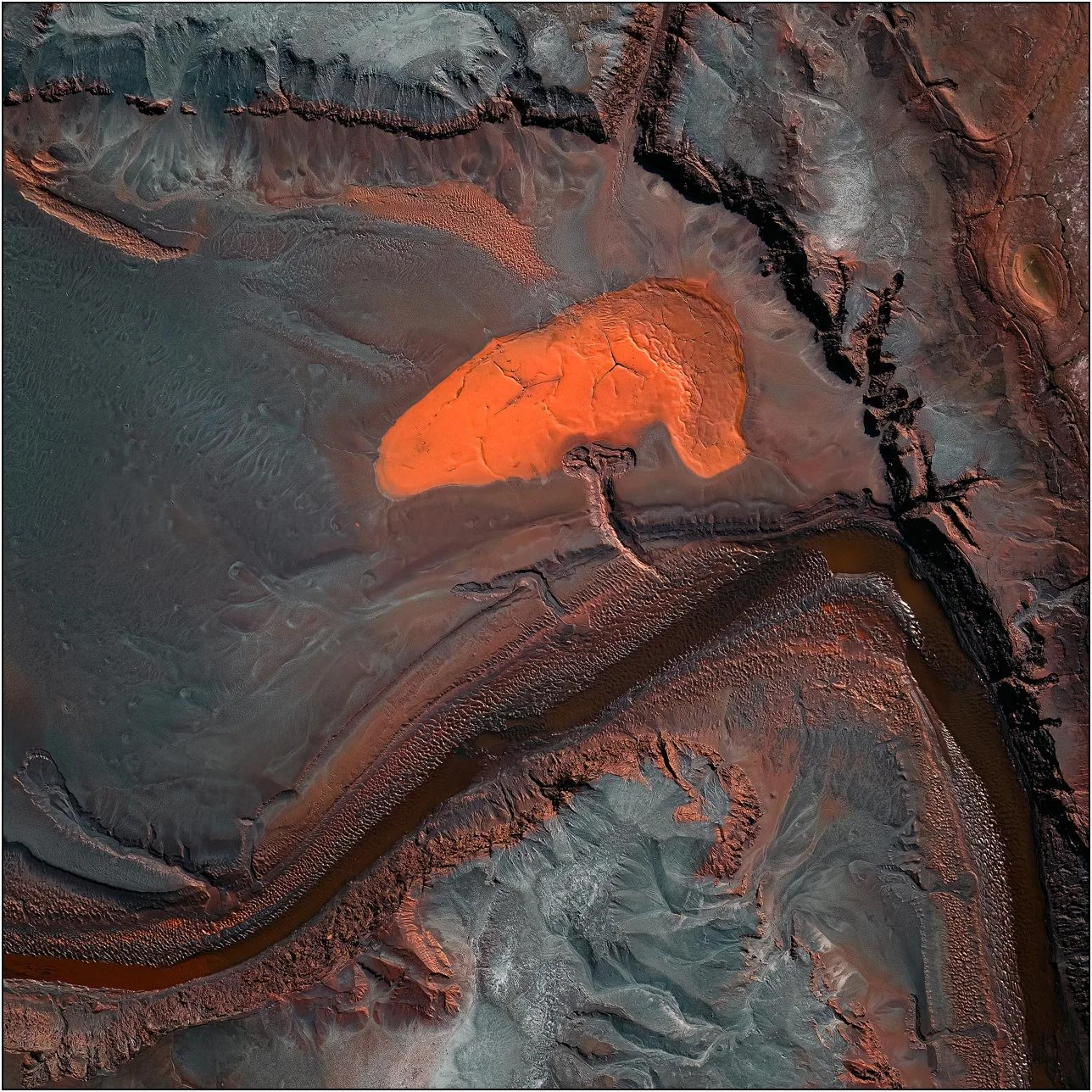 Aerial view of a tailings lake with converging mineral streams and textured deposits