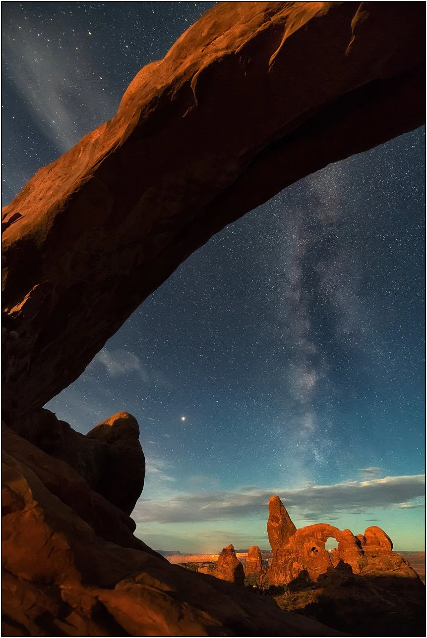 Natural rock arch under the Milky Way frames another arch in Arches National Park.