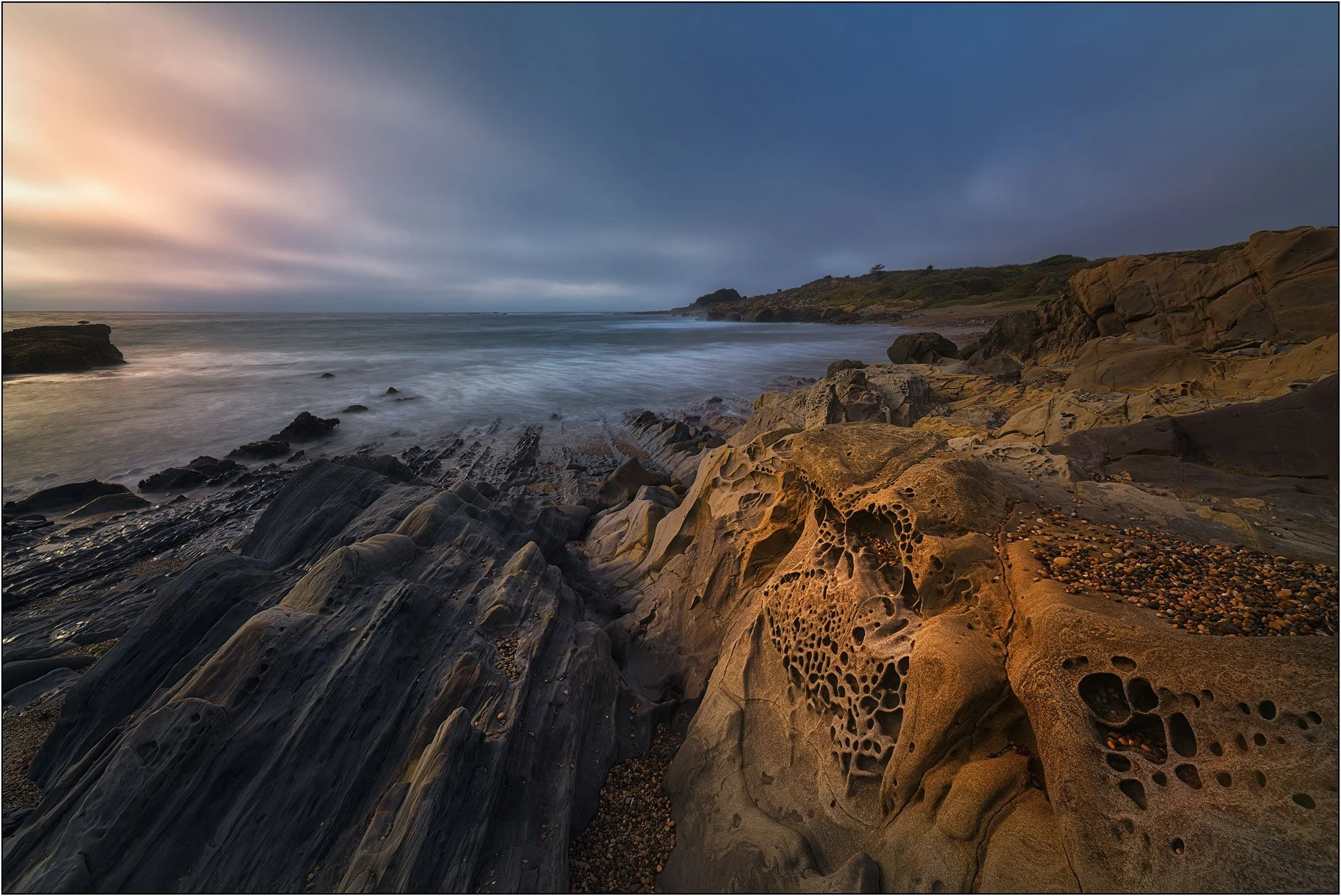 Tafoni rock formations along a quiet coastline at dusk