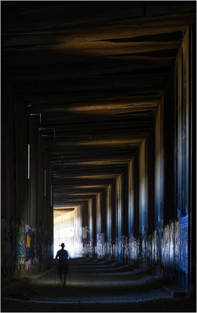 Figure walking through a tunnel with repeating structure and light