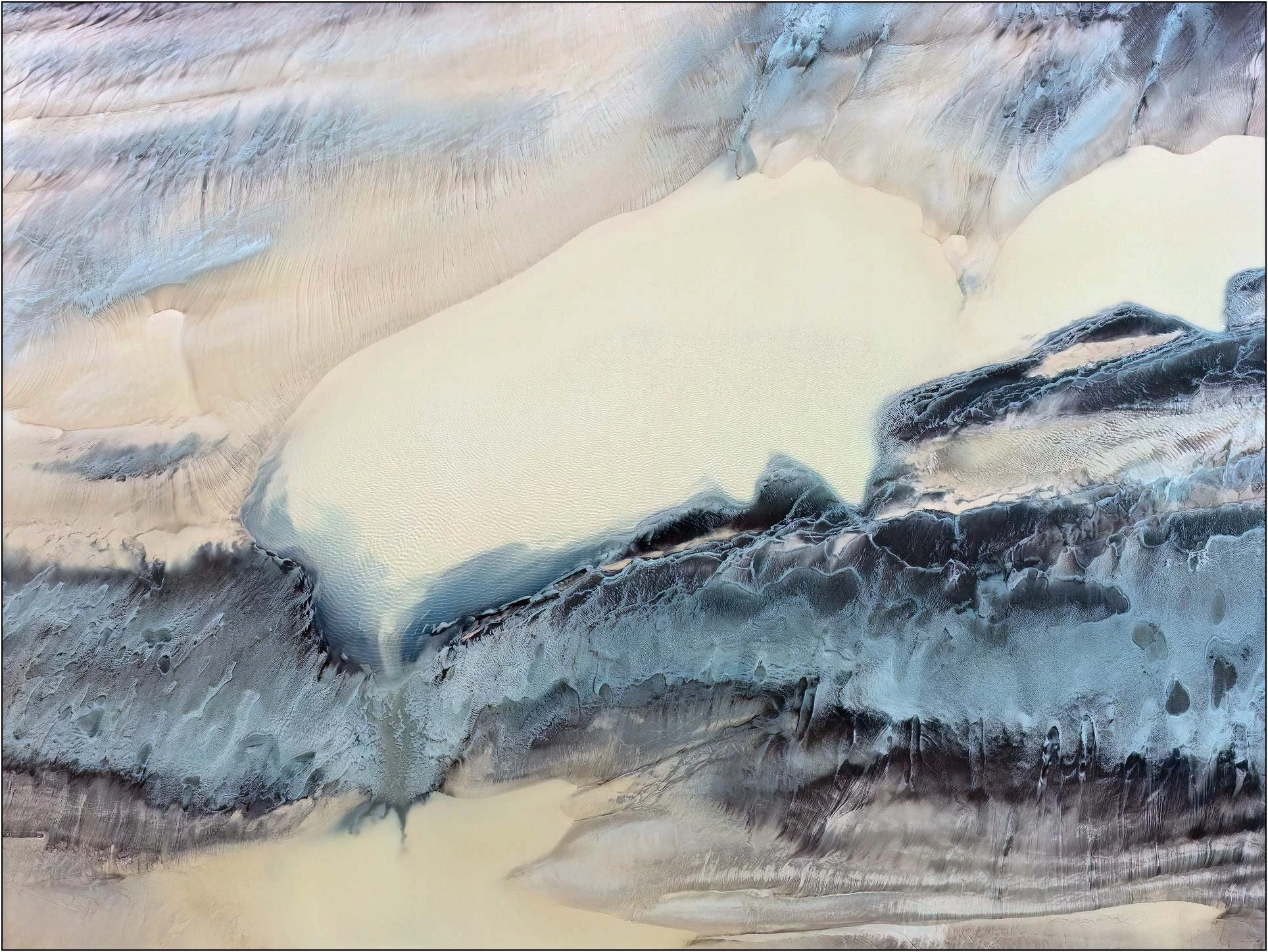 Abstract aerial photography of the Qiantang River tidal flats in China, where tidal currents shape pale sand and blue-gray sediment into sweeping organic forms. Expansive negative space surrounds a dark, mountain-like ridge, creating a minimalist com