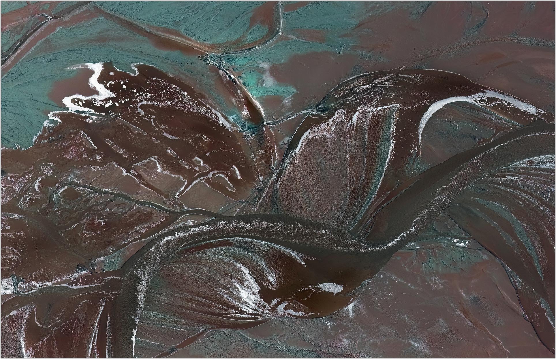 Aerial view of a tailings lake with sweeping curved channels and textured mineral surfaces