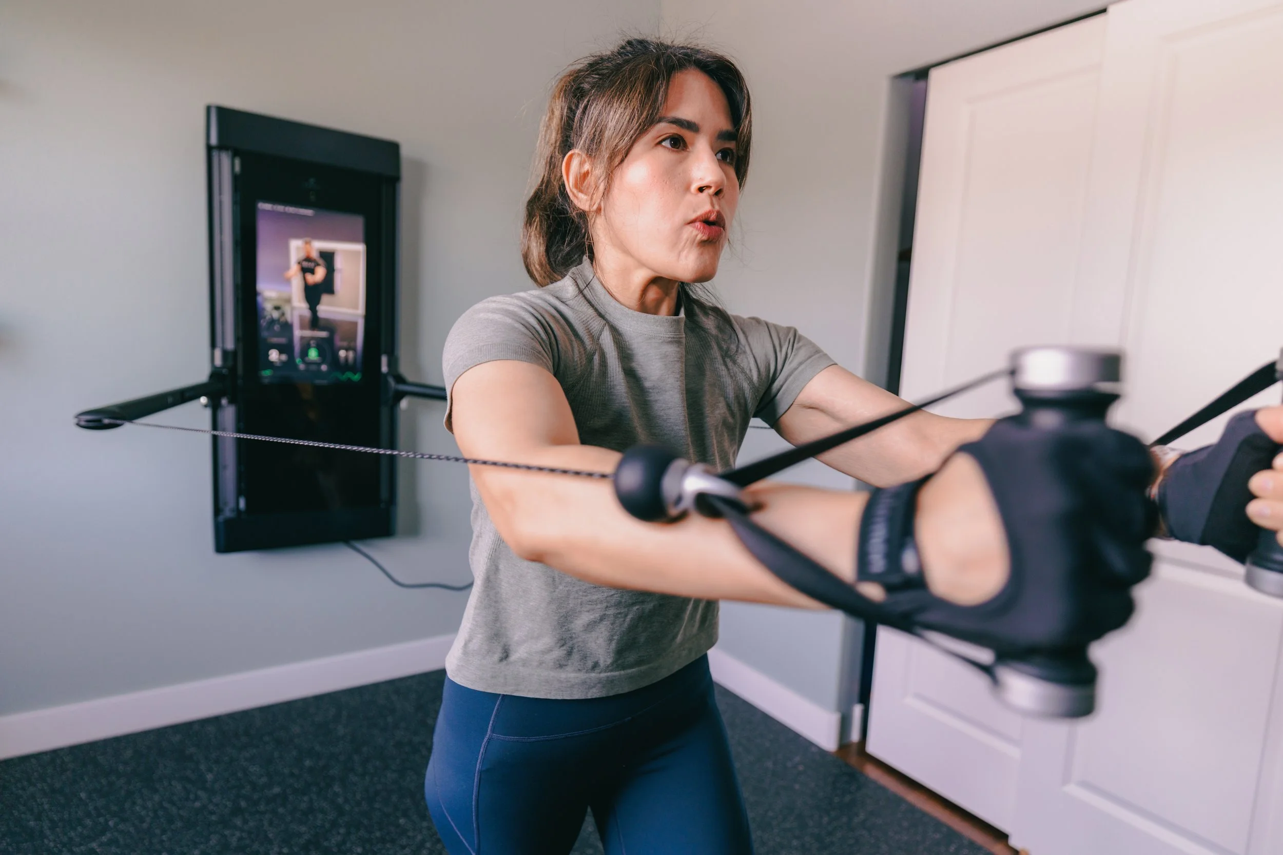 Woman exercising on a fitness machine with a screen in the background.