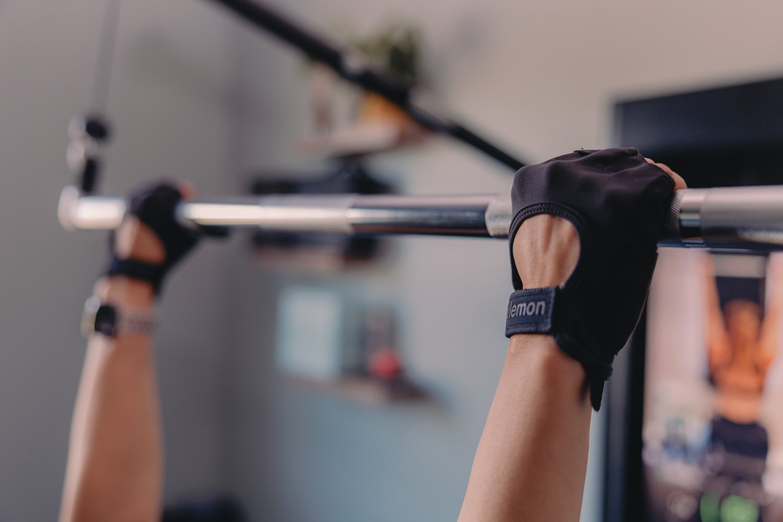Close-up of a person lifting a barbell with black weightlifting gloves, in a gym setting.