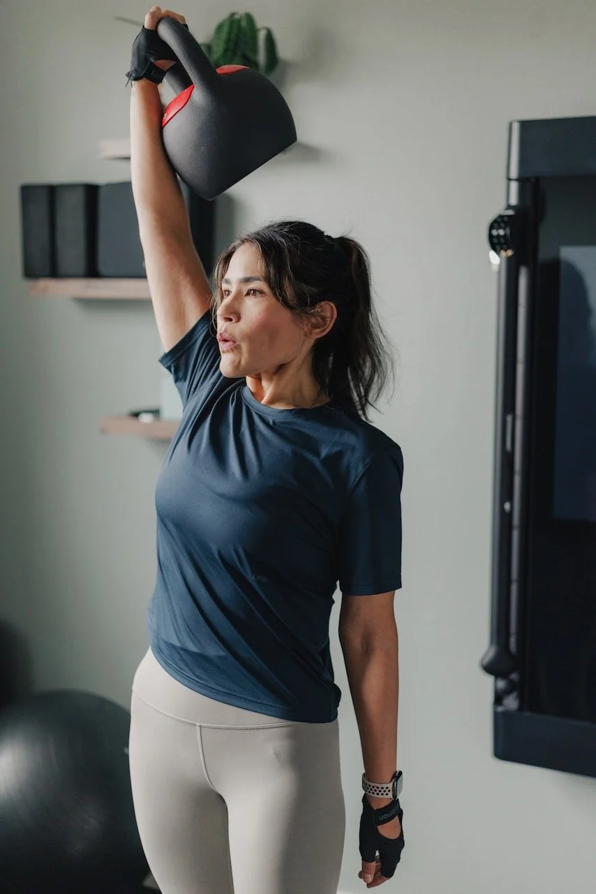 Woman lifting a kettlebell in a fitness room with exercise equipment in the background.