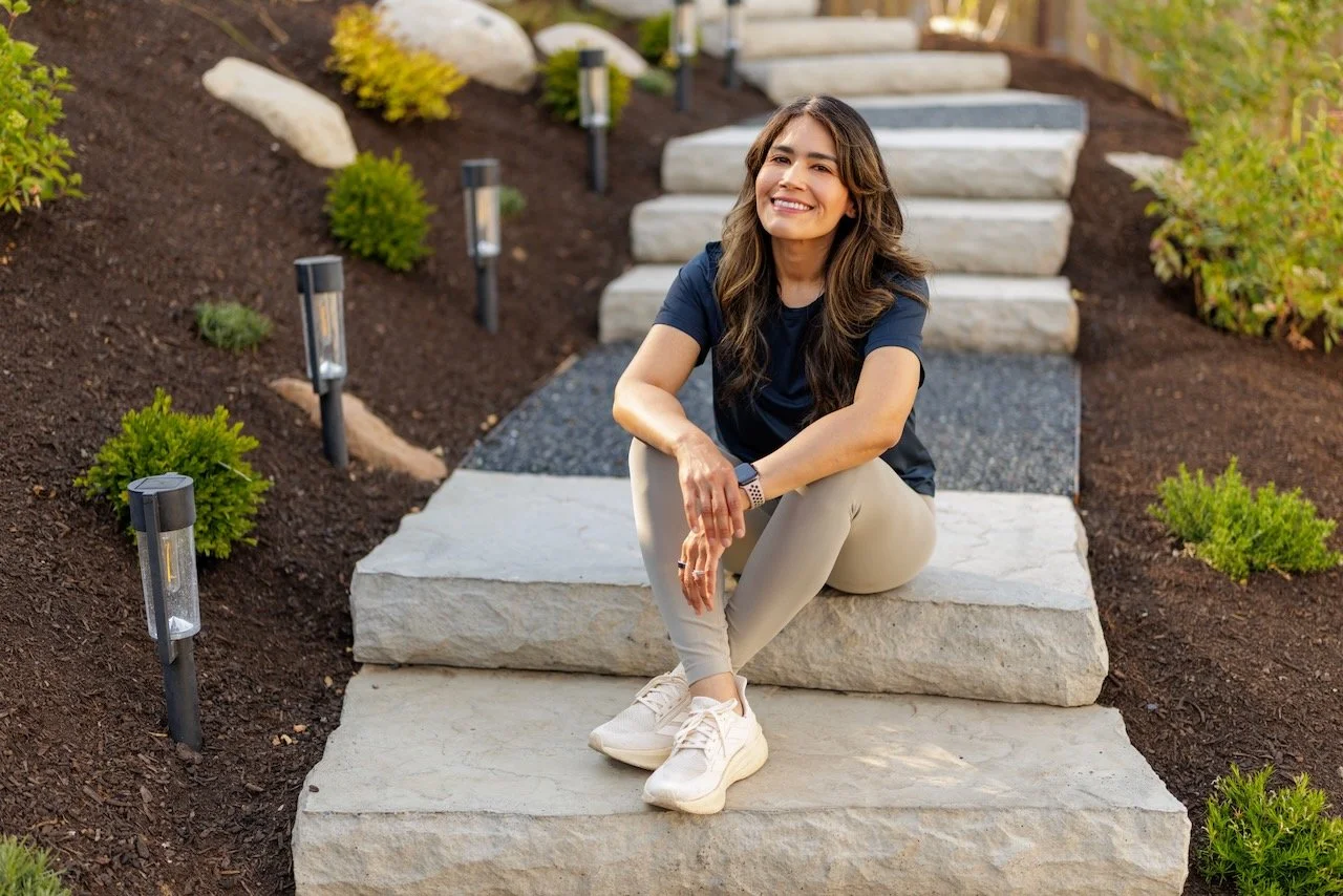 A woman smiling and sitting on outdoor stone steps surrounded by landscaped garden with small bushes and pathway lights.