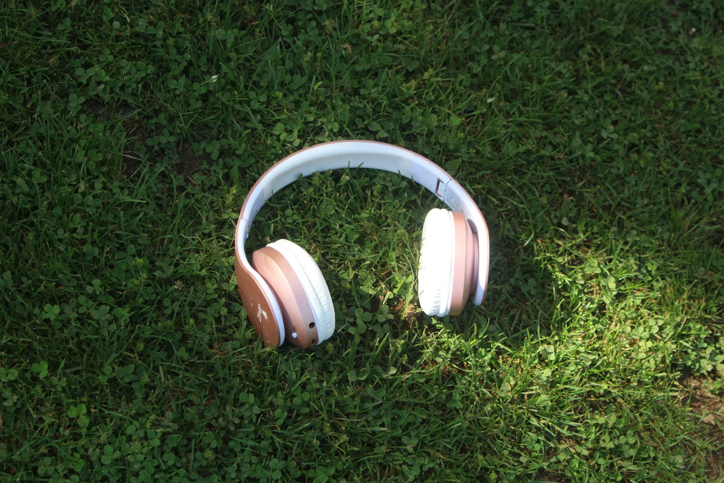 A pair of pink and white over-ear headphones resting on green grass.