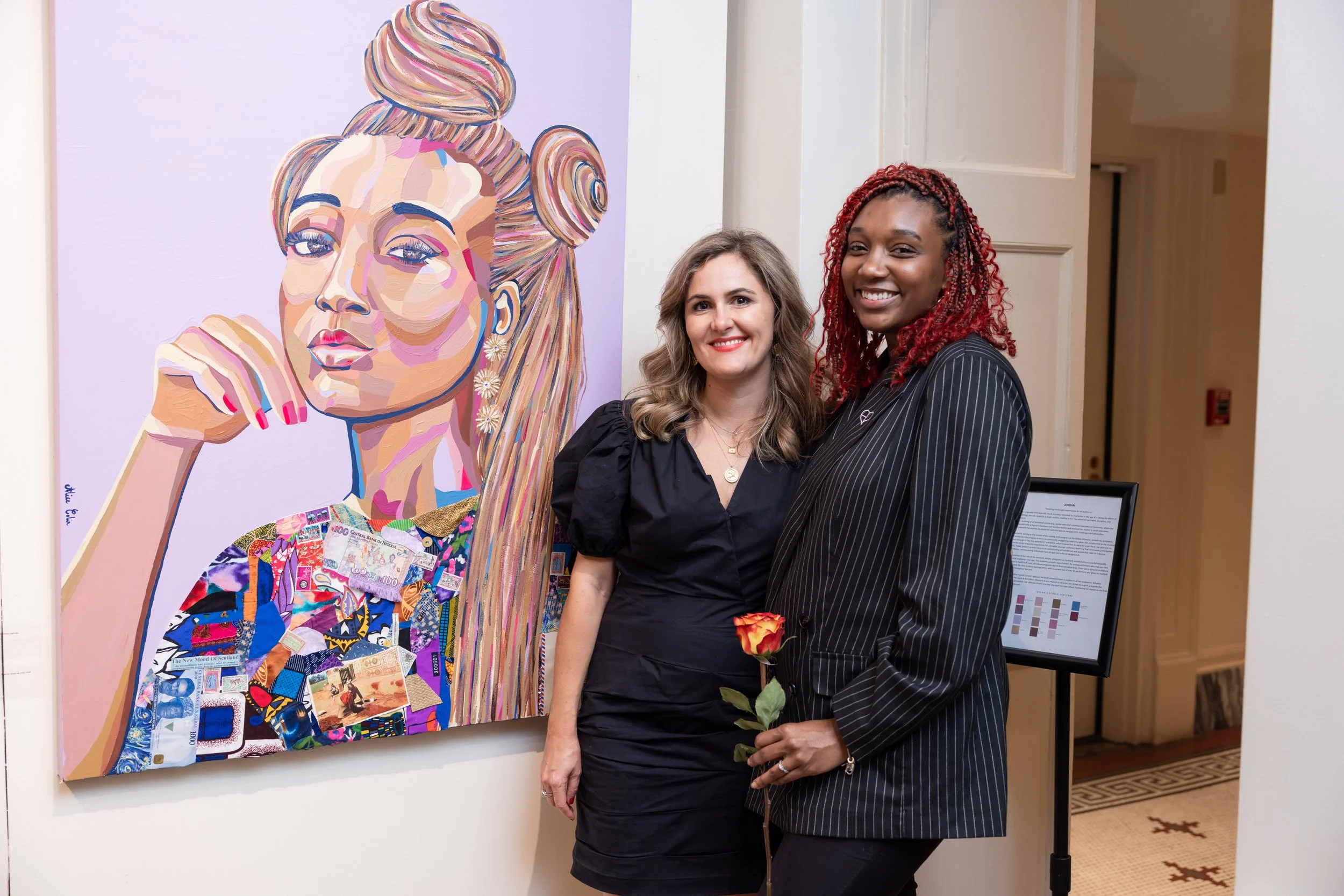 Two women smiling, standing next to a colorful portrait of a woman with bun hairstyle, wearing earrings and holding a rose, art piece includes collage of various images and currency notes.